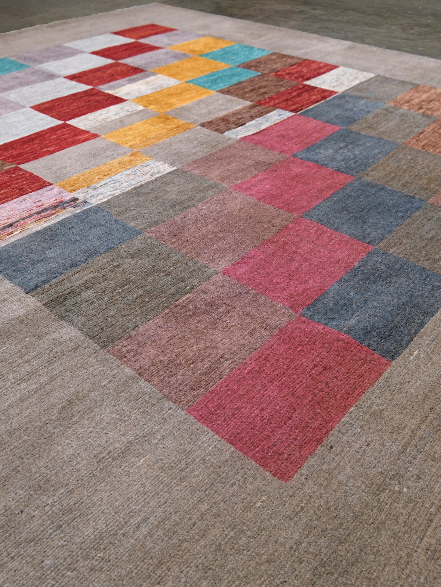 A square area rug with a patchwork design of colored squares on a beige base, photographed from an elevated angle.