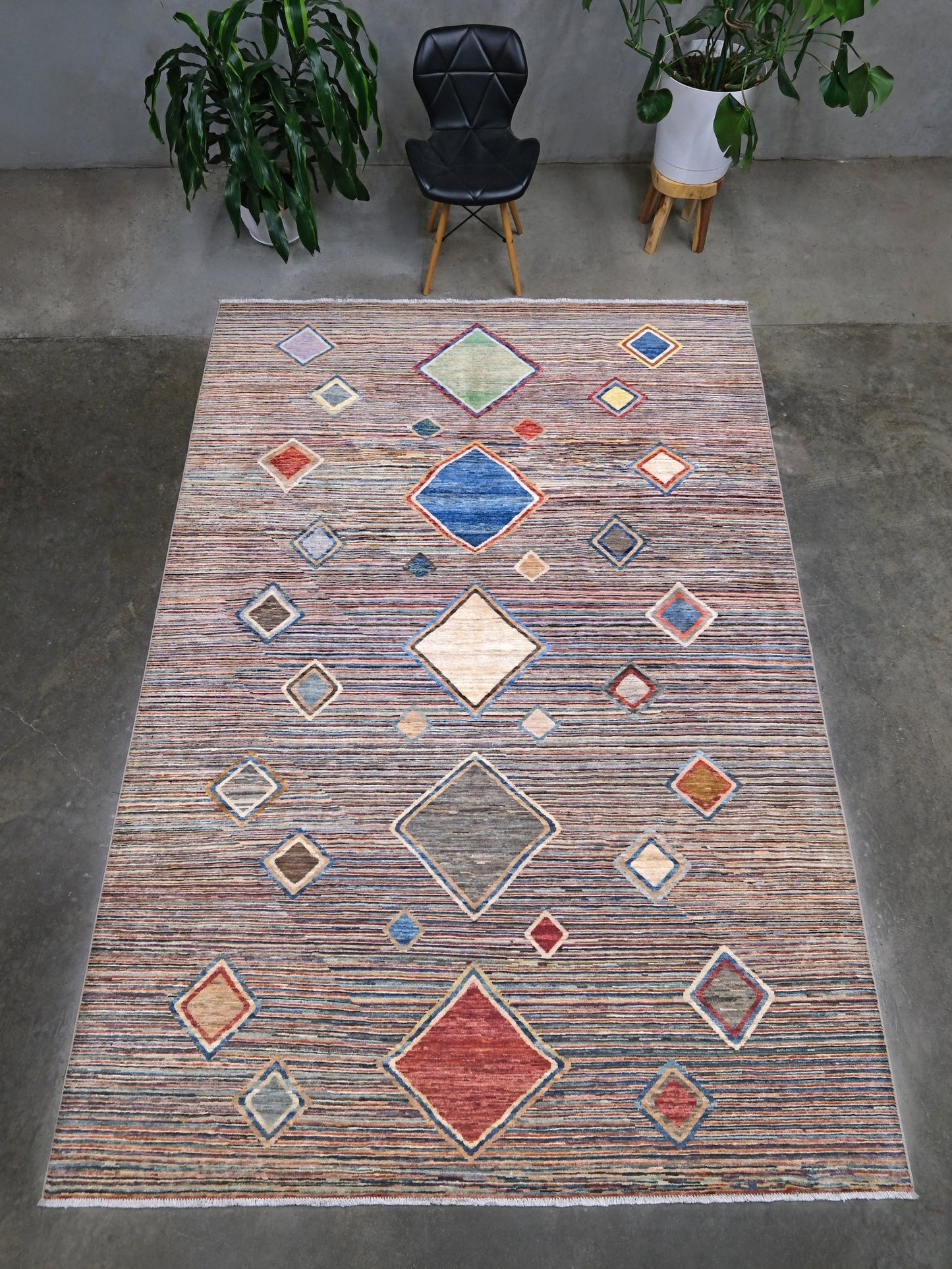 A rectangular area rug with a textured, distressed pattern in muted tones of blue, red, beige, and brown, featuring a central diamond motif and smaller diamond accents. Modern Turkish Gabbeh style handmade wool rug with colorful diamond medallions on a striped field in blue, red, ivory, gray, green, camel and lavender, 7x10 from Indigo Rugs Burlingame Bay Area.