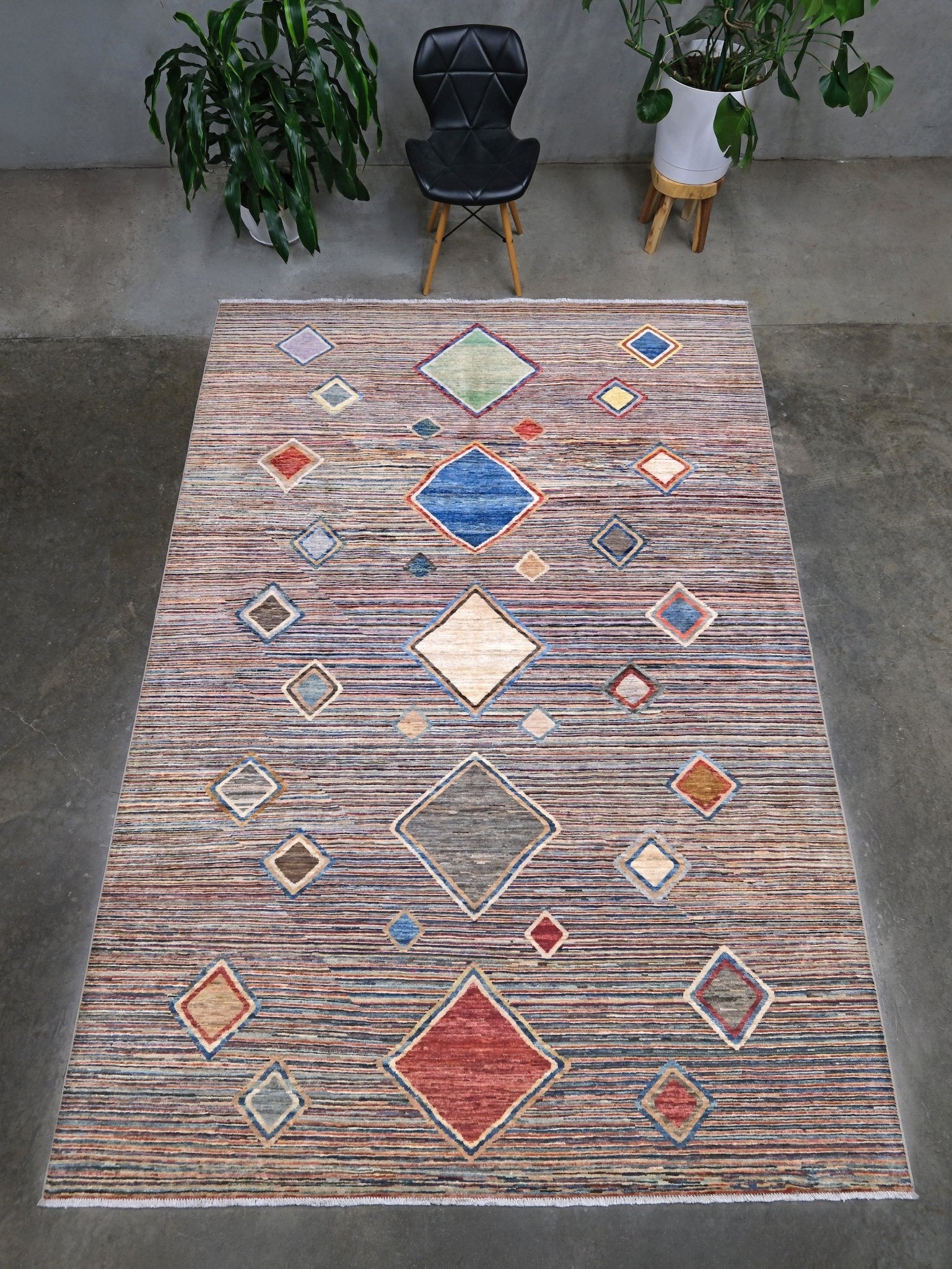 A rectangular area rug with a textured, distressed pattern in muted tones of blue, red, beige, and brown, featuring a central diamond motif and smaller diamond accents. Modern Turkish Gabbeh style handmade wool rug with colorful diamond medallions on a striped field in blue, red, ivory, gray, green, camel and lavender, 7x10 from Indigo Rugs Burlingame Bay Area.