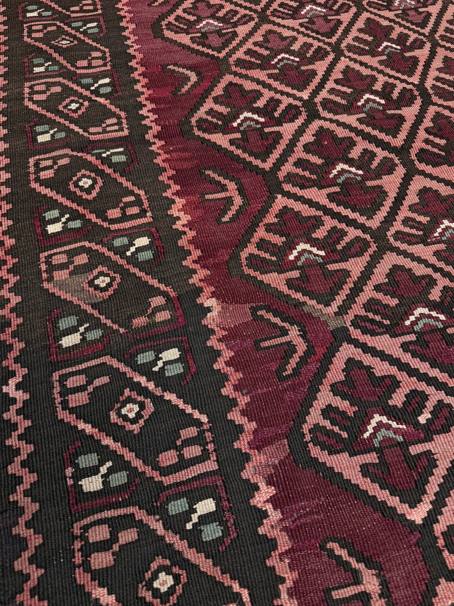 Close-up of a patterned fabric with geometric design. Vintage Caucasian kilim rug with wine red and dusty rose lattice field and tribal animal motifs, handwoven wool flatweave 5x10 runner size from Indigo Rugs Burlingame California