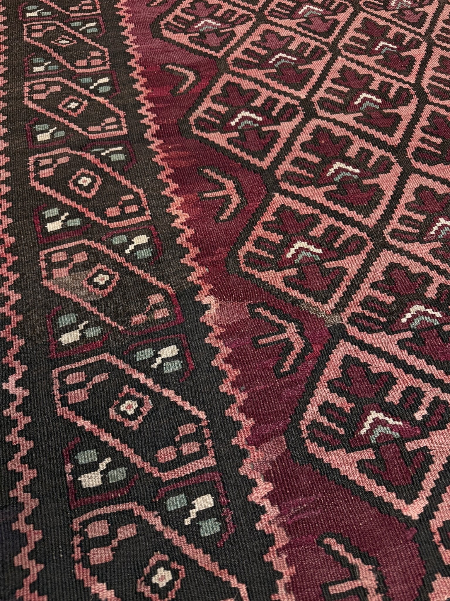 Close-up of a patterned fabric with geometric design. Vintage Caucasian kilim rug with wine red and dusty rose lattice field and tribal animal motifs, handwoven wool flatweave 5x10 runner size from Indigo Rugs Burlingame California