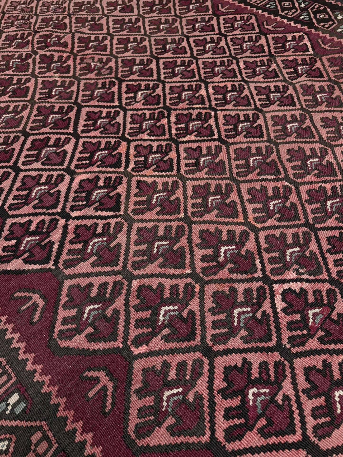 Close-up of a patterned fabric with geometric design. Vintage Caucasian kilim rug with wine red and dusty rose lattice field and tribal animal motifs, handwoven wool flatweave 5x10 runner size from Indigo Rugs Burlingame California