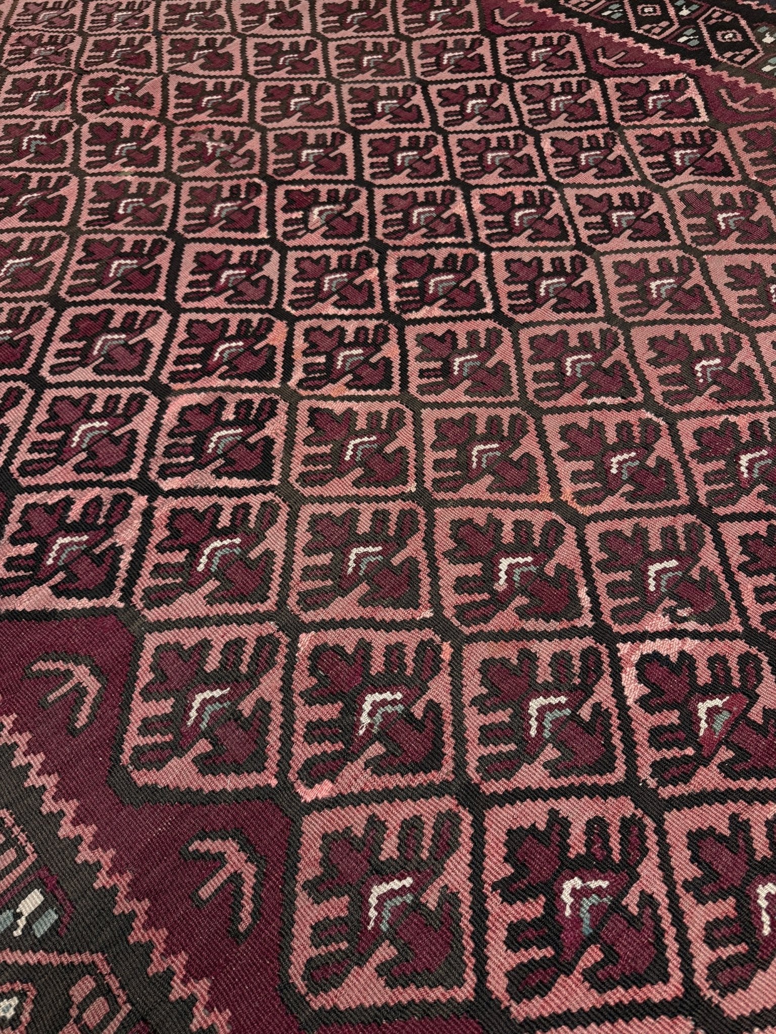 Close-up of a patterned fabric with geometric design. Vintage Caucasian kilim rug with wine red and dusty rose lattice field and tribal animal motifs, handwoven wool flatweave 5x10 runner size from Indigo Rugs Burlingame California