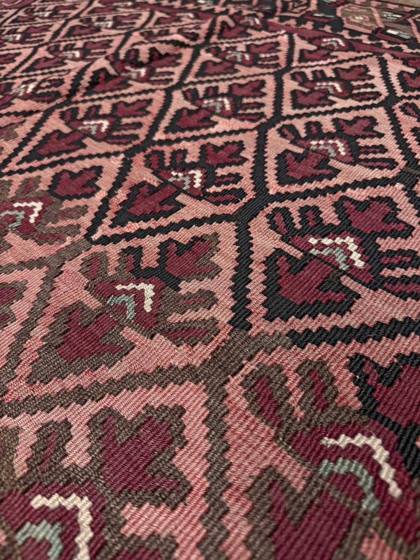 Close-up of a patterned fabric with geometric design. Vintage Caucasian kilim rug with wine red and dusty rose lattice field and tribal animal motifs, handwoven wool flatweave 5x10 runner size from Indigo Rugs Burlingame California