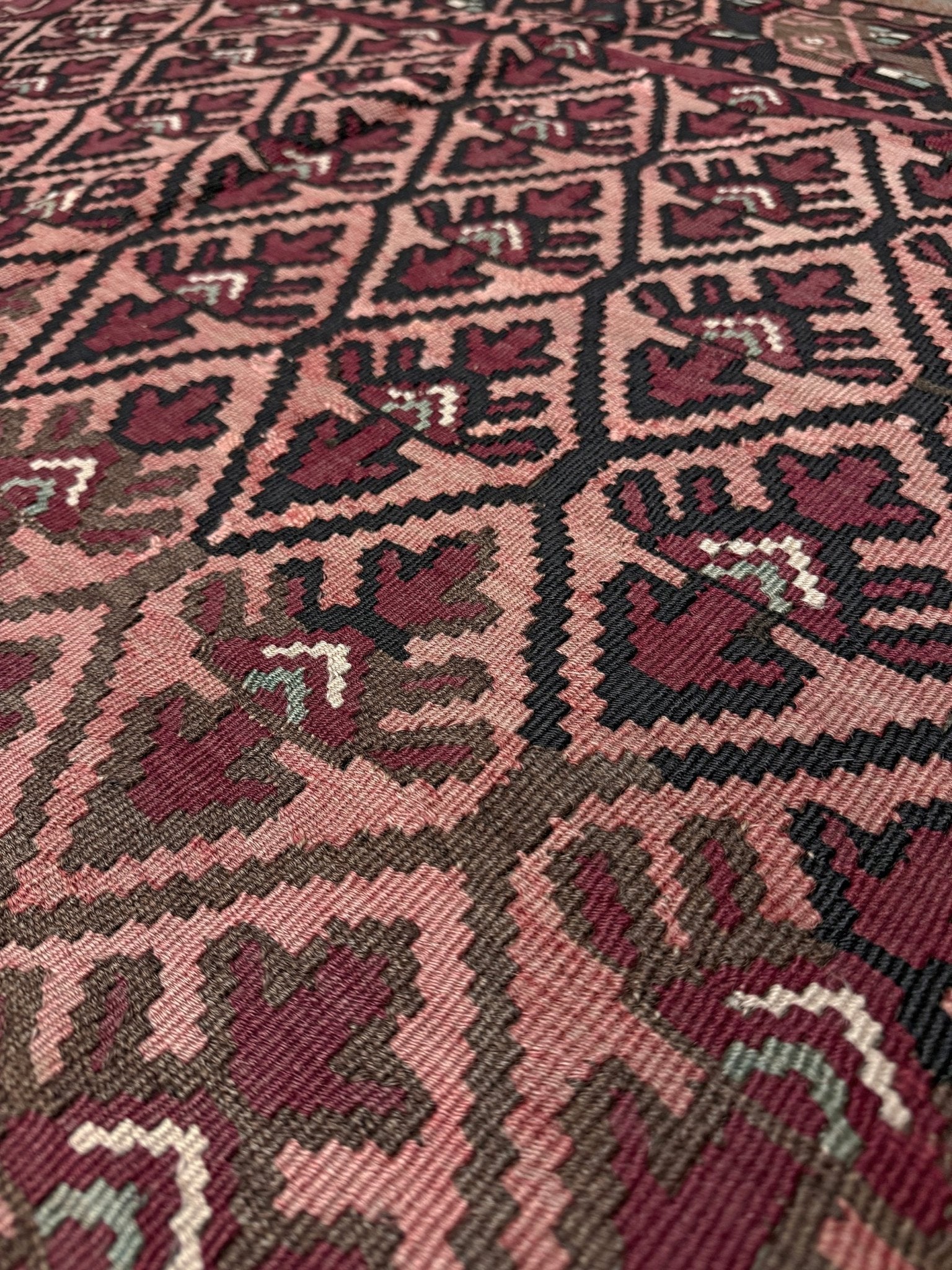 Close-up of a patterned fabric with geometric design. Vintage Caucasian kilim rug with wine red and dusty rose lattice field and tribal animal motifs, handwoven wool flatweave 5x10 runner size from Indigo Rugs Burlingame California