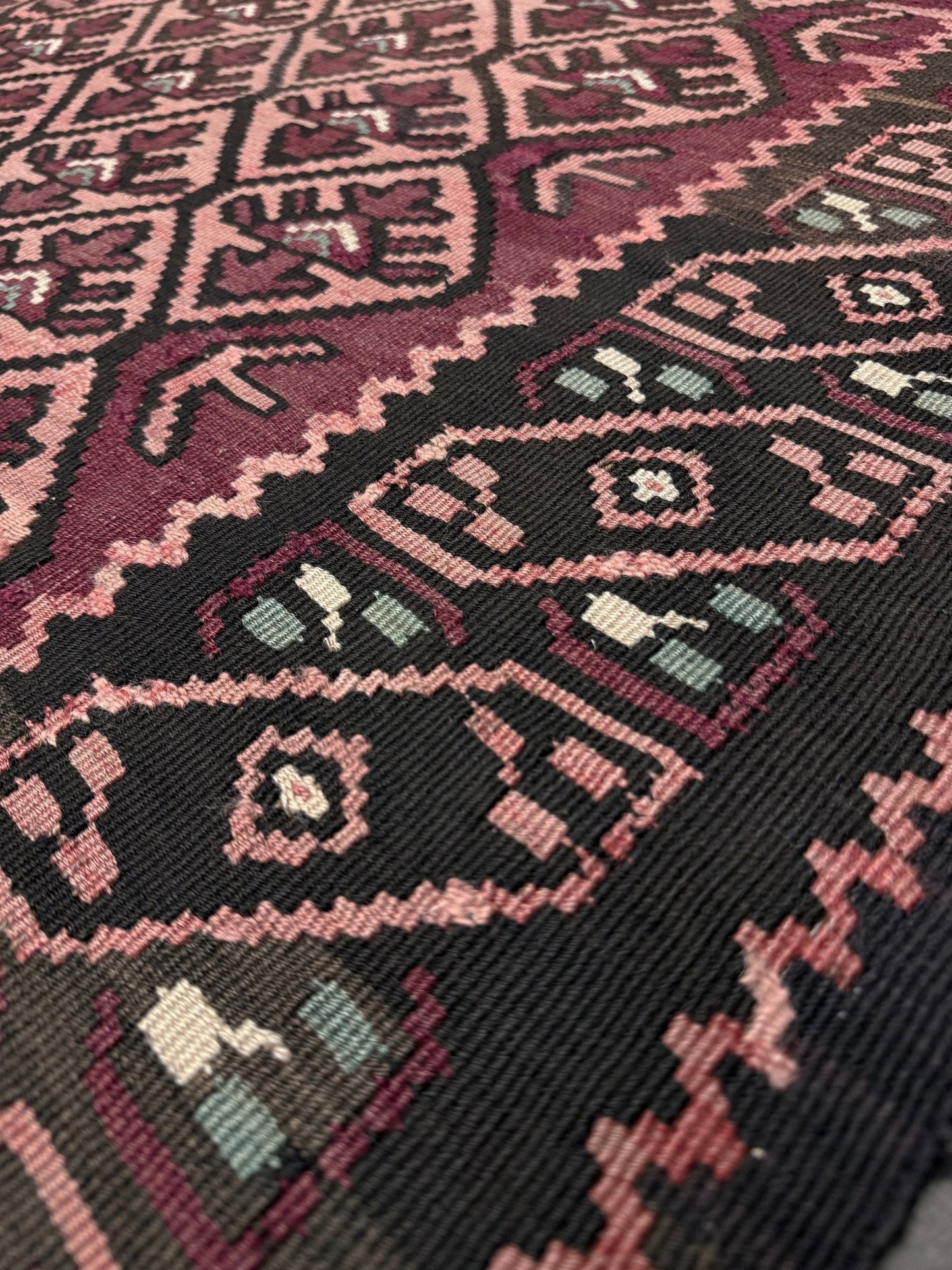 Close-up of a patterned fabric with intricate designs in red, black, and beige. Vintage Caucasian kilim rug with wine red and dusty rose lattice field and tribal animal motifs, handwoven wool flatweave 5x10 runner size from Indigo Rugs Burlingame California