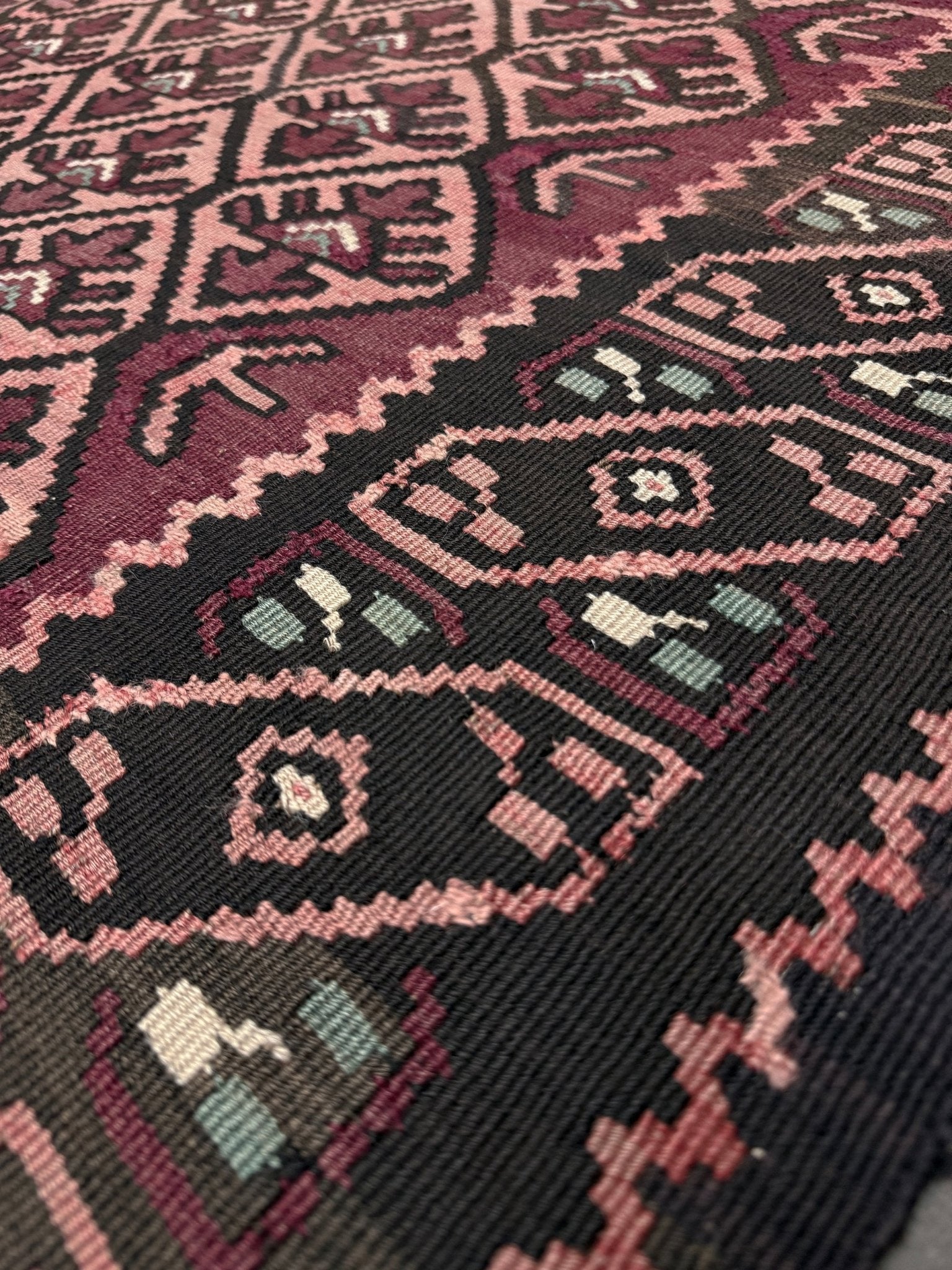 Close-up of a patterned fabric with intricate designs in red, black, and beige. Vintage Caucasian kilim rug with wine red and dusty rose lattice field and tribal animal motifs, handwoven wool flatweave 5x10 runner size from Indigo Rugs Burlingame California