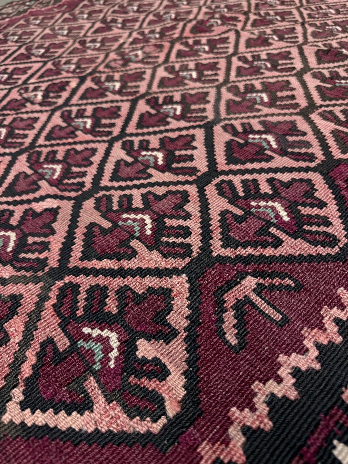 Close-up of a patterned fabric with geometric design. Vintage Caucasian kilim rug with wine red and dusty rose lattice field and tribal animal motifs, handwoven wool flatweave 5x10 runner size from Indigo Rugs Burlingame California