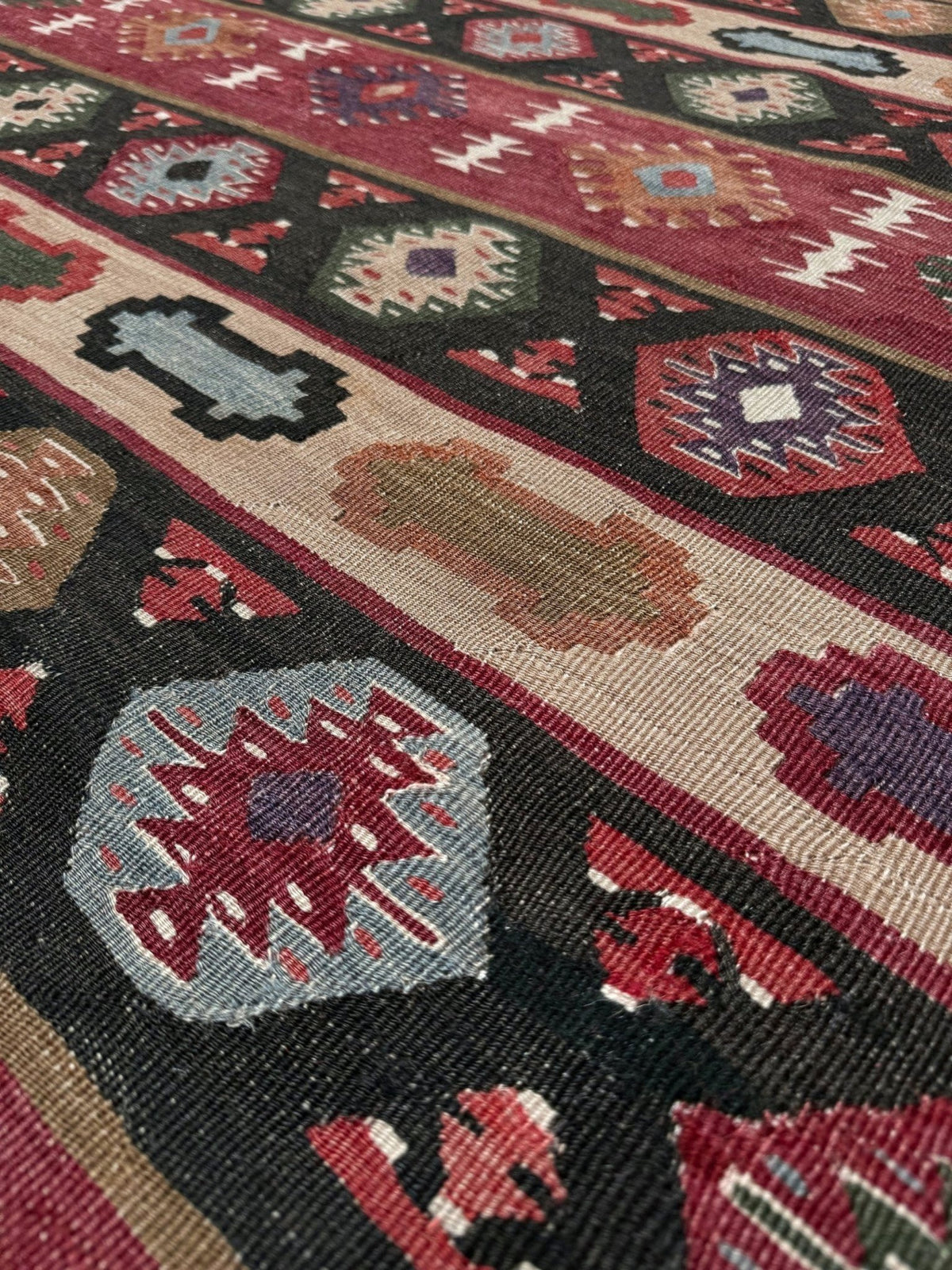 A close-up of a woven geometric rug with a dark charcoal base, red and beige borders, and multicolored tribal-style motifs including hexagons and diamonds.