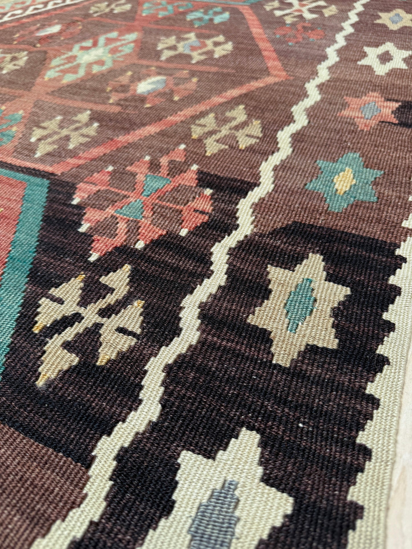 Close-up of a patterned rug with geometric designs in brown, green, and beige. Vintage Kayseri Turkish kilim rug with earthy colors and geometric design, handmade wool flatweave 5x11 from Indigo Rugs Burlingame Bay Area.