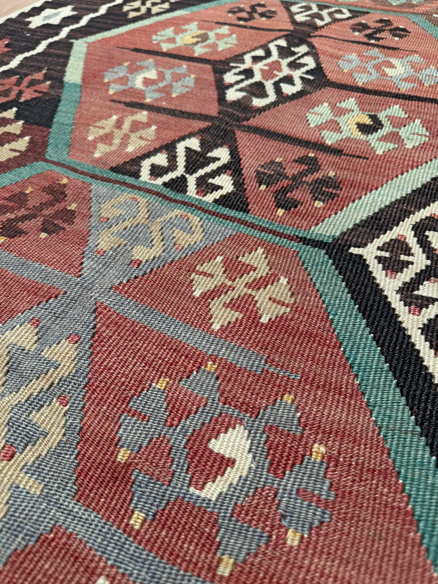 Close-up of a patterned rug with geometric designs in red, blue, and black. Vintage Kayseri Turkish kilim rug with earthy colors and blue-gray geometric medallions, handmade wool flatweave 5x11 from Indigo Rugs Burlingame Bay Area.