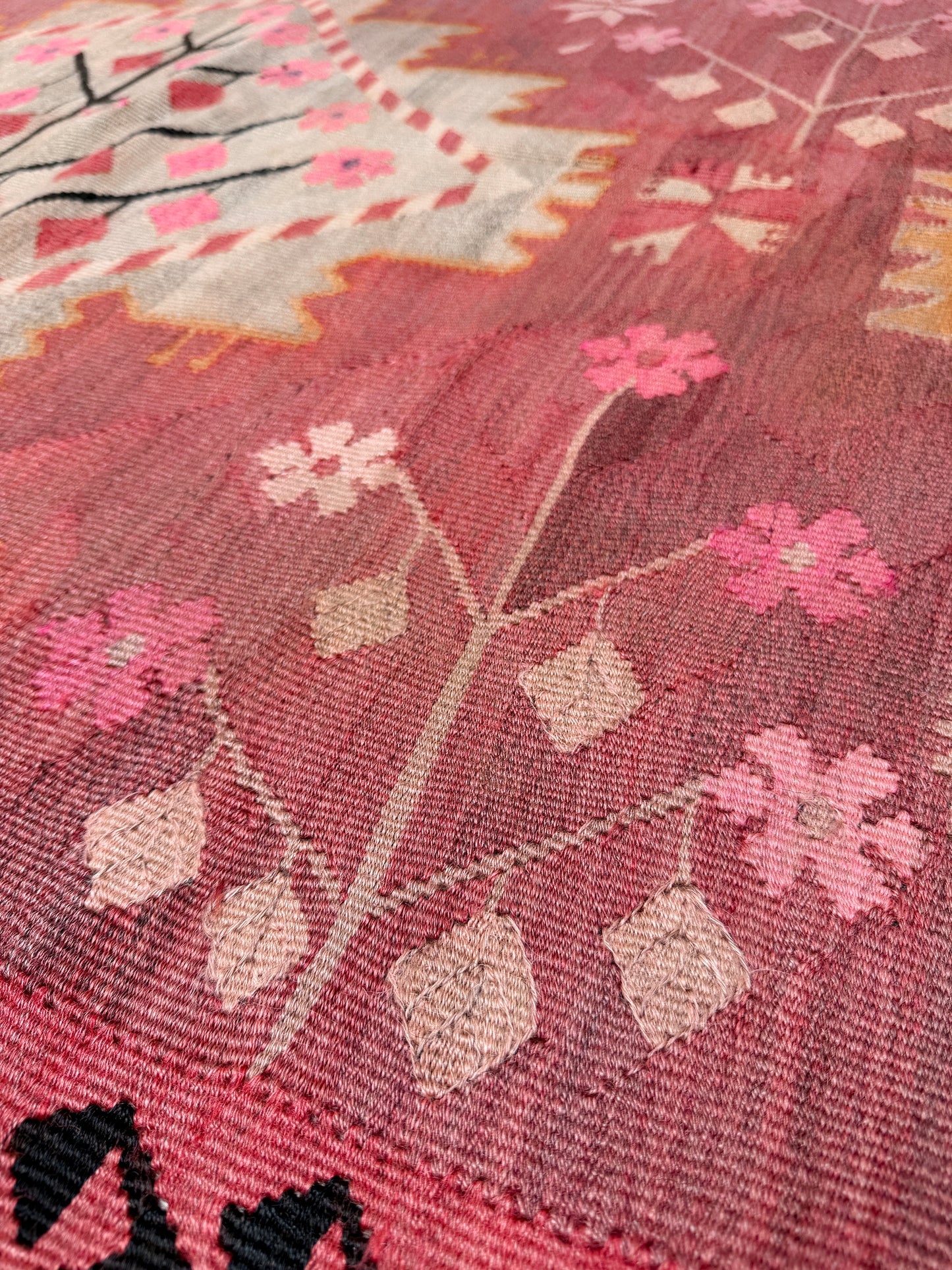 Close-up of a textured fabric with floral patterns in pink, white, and black. Vintage Kars Turkish kilim rug in dusty pink, warm apricot orange, handwoven from Anatolian wool 5x10. 