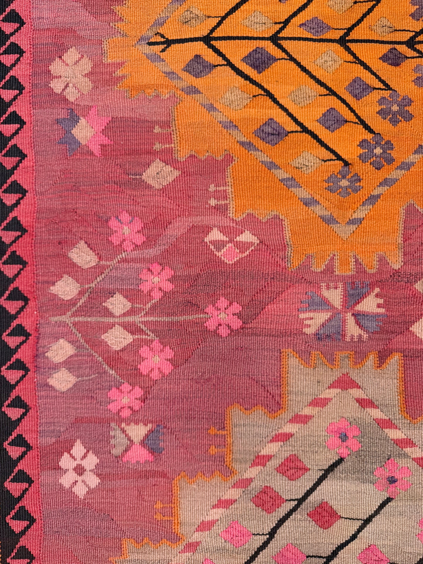 Close-up of a colorful patterned fabric with geometric and floral designs. Vintage Kars Turkish kilim rug in dusty pink, warm apricot orange, handwoven from Anatolian wool 5x10. 