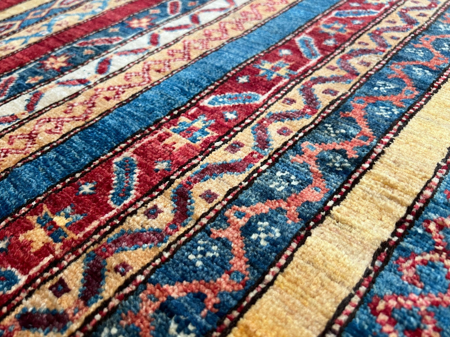 Close up Handmade Turkish Shawl Rug with vibrant vertical stripes in red, blue, yellow, and cream, featuring intricate tribal motifs from the best luxury rug shop in the San Francisco Bay Area. High-quality wool rug at an affordable price with free shipping. Perfect for adding a touch of Turkish craftsmanship to any room. Ideal statement piece for living rooms, bedrooms, and entryways.