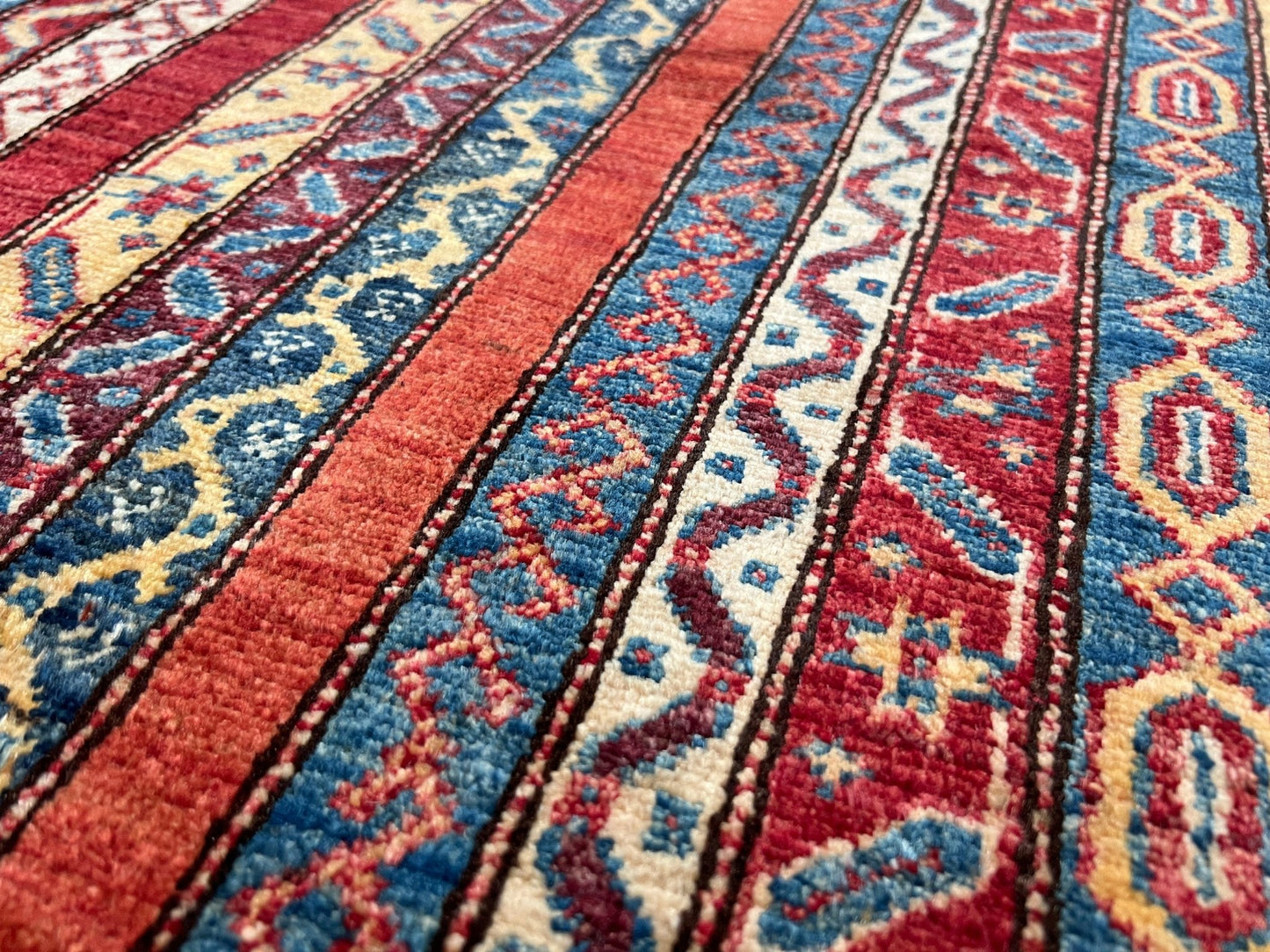 Close up Handmade Turkish Shawl Rug with vibrant vertical stripes in red, blue, yellow, and cream, featuring intricate tribal motifs from the best luxury rug shop in the San Francisco Bay Area. High-quality wool rug at an affordable price with free shipping. Perfect for adding a touch of Turkish craftsmanship to any room. Ideal statement piece for living rooms, bedrooms, and entryways.