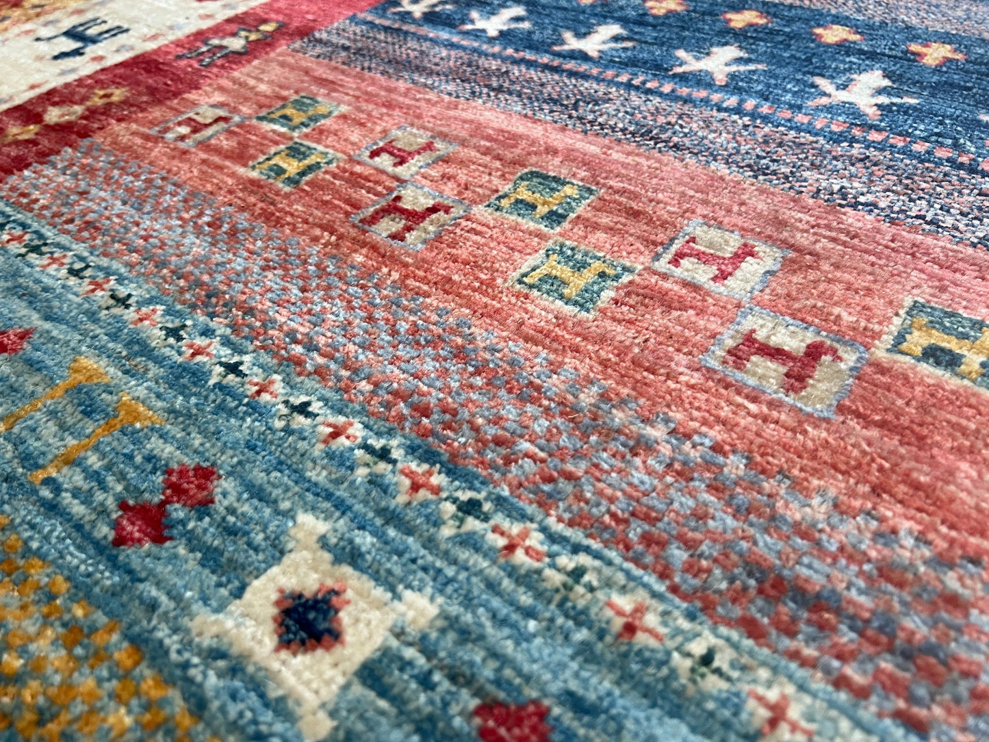 Close up of Colorful handmade Gabbeh rug with animal motifs in rich brick red, soft sky blue, teal, golden mustard yellow, forest green, and cream hues from the best luxury handmade rug shop in the San Francisco Bay Area. Premium quality wool rug featuring vibrant stripes and tribal design elements. Perfect as a statement piece for living rooms and cozy spaces. Free shipping available.