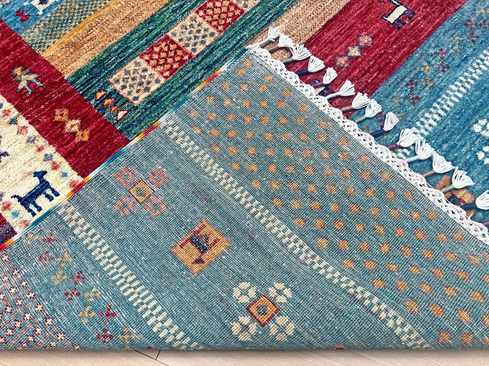 Back of Colorful handmade Gabbeh rug with animal motifs in rich brick red, soft sky blue, teal, golden mustard yellow, forest green, and cream hues from the best luxury handmade rug shop in the San Francisco Bay Area. Premium quality wool rug featuring vibrant stripes and tribal design elements. Perfect as a statement piece for living rooms and cozy spaces. Free shipping available.