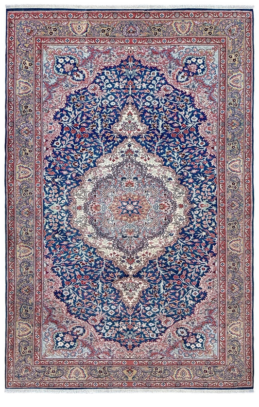 A traditional Persian-style area rug with a central medallion, featuring a dominant navy blue field, a dusty pink border, and cream and red accents in an intricate floral and vine pattern. Blue vintage Turkish rug with deep blue field,  floral medallion, handmade wool 7x9 from Indigo Rugs Burlingame Bay Area.