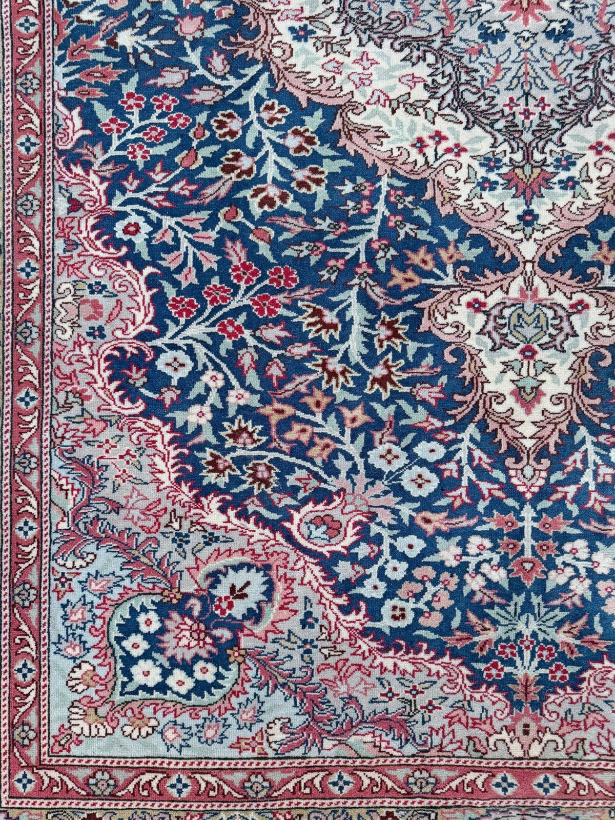 A close-up of an ornate Persian-style area rug featuring a deep blue field, intricate floral motifs in red, pink, and cream, and a detailed decorative border. Blue vintage Turkish rug with deep blue field,  floral medallion, handmade wool 7x9 from Indigo Rugs Burlingame Bay Area.