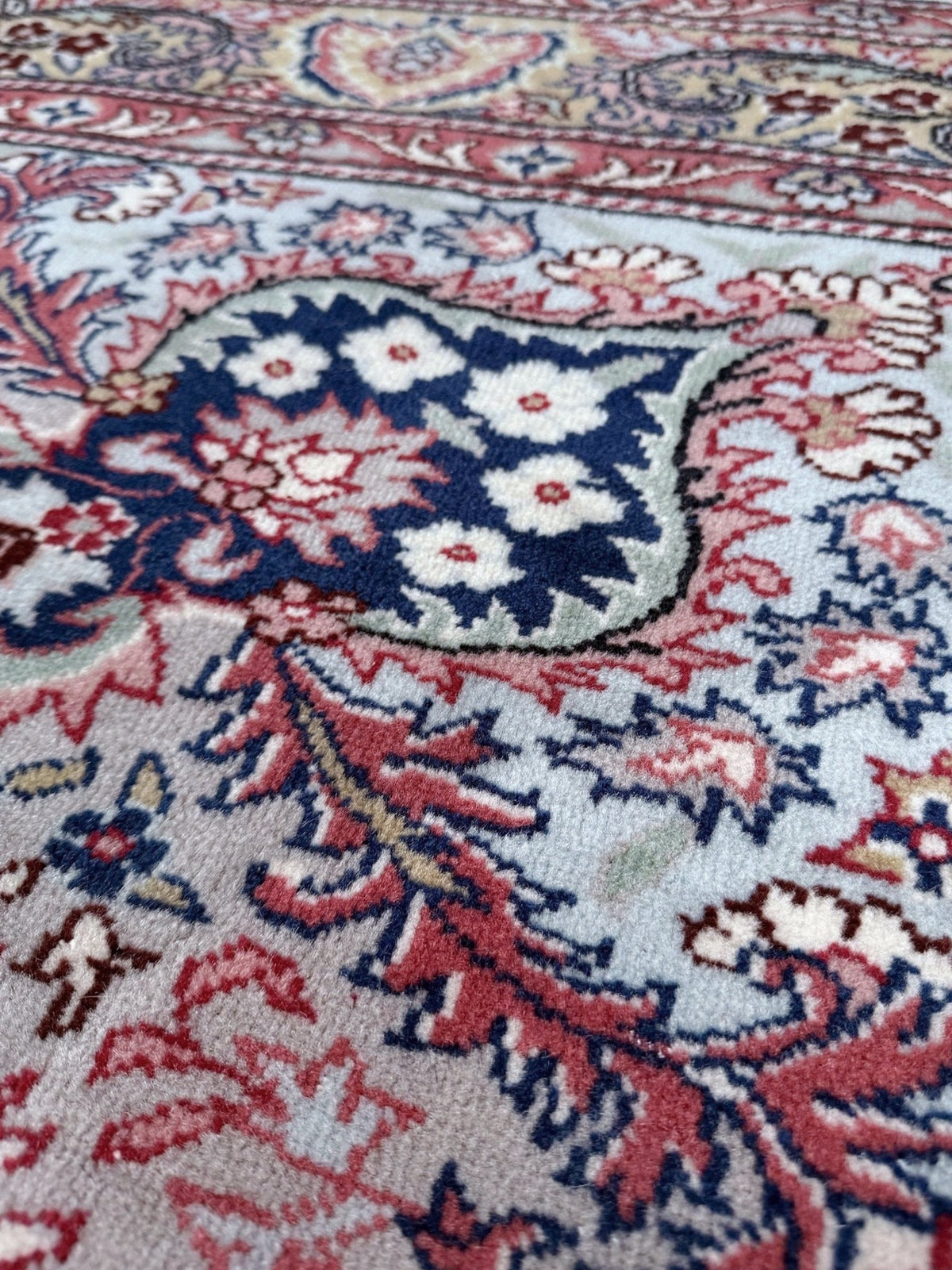 A close-up of a traditional patterned rug with a cream base, featuring red, navy blue, and white floral motifs. Blue vintage Turkish rug with deep blue field,  floral medallion, handmade wool 7x9 from Indigo Rugs Burlingame Bay Area.