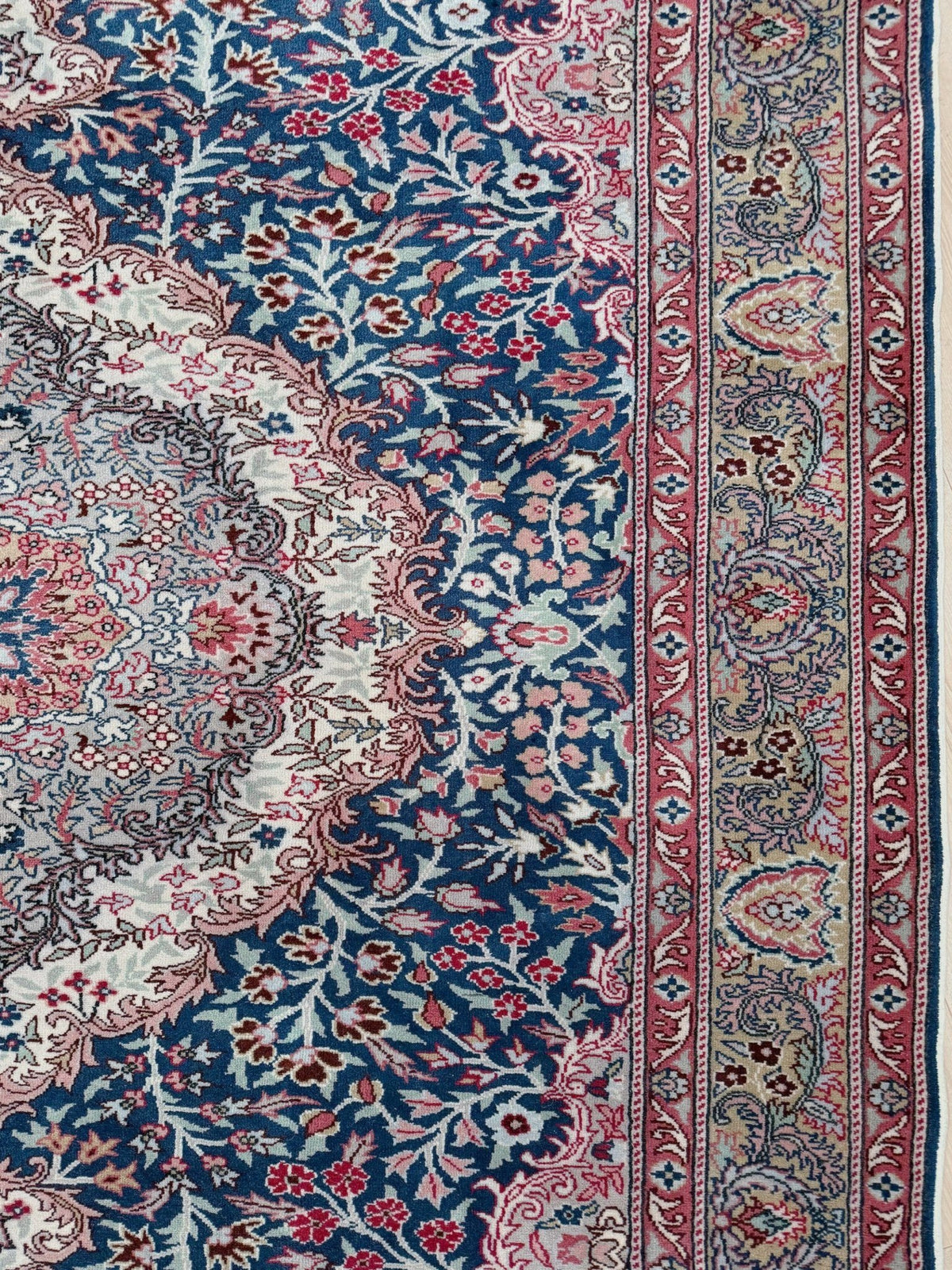 A close-up of a traditional patterned rug showing a navy blue field with red, pink, and beige floral motifs, a large central medallion, and a detailed border.