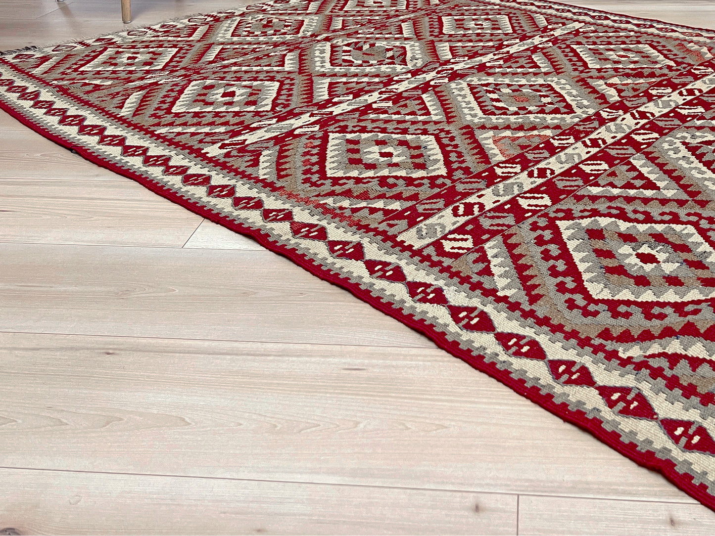 Decorative red and beige patterned rug on a wooden floor with a chair and plants in the background. Vintage kurdish van kilim rug 5x8 red beige geometric flatweave eastern anatolia handmade wool tribal rug.