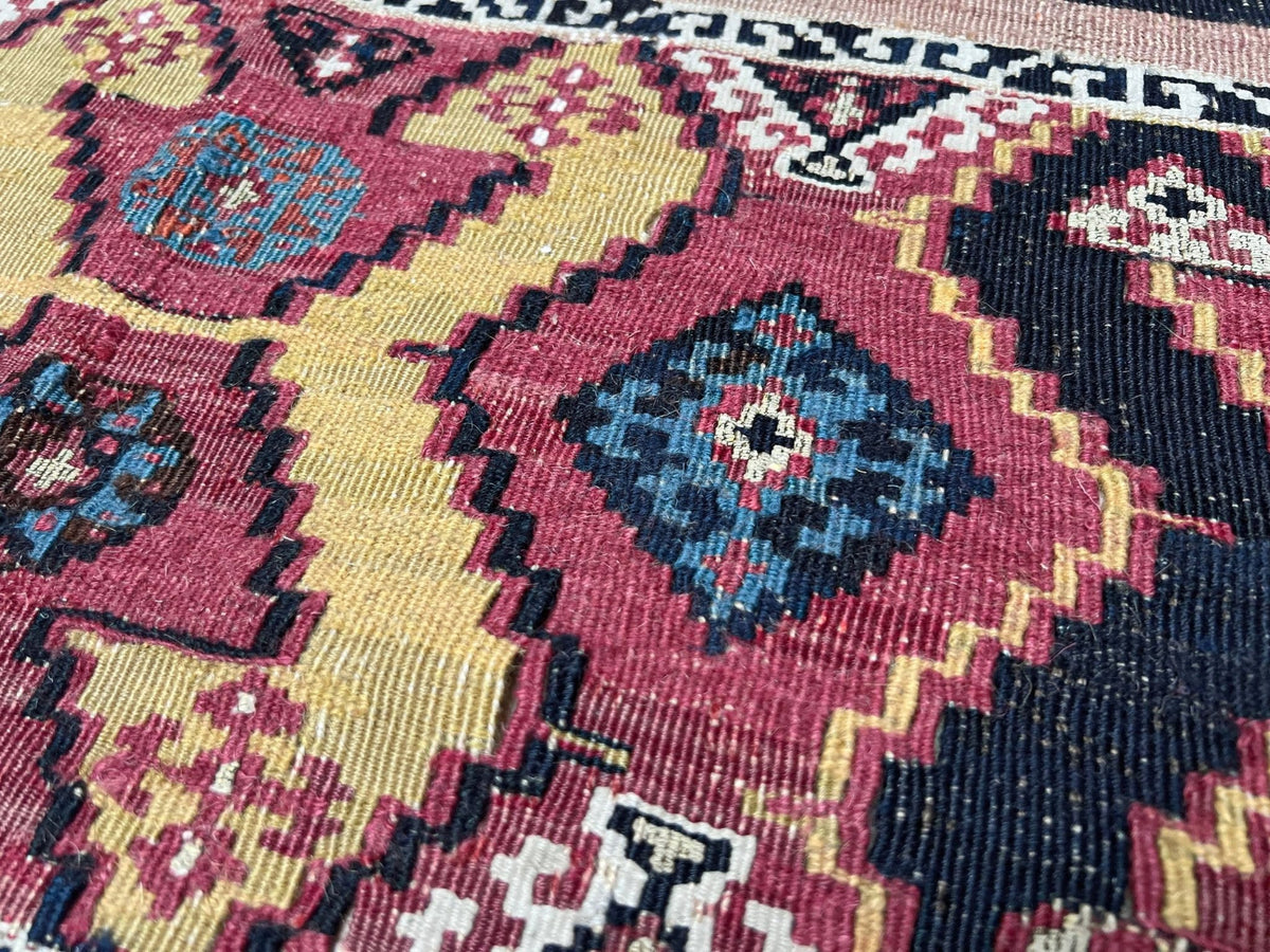 Close-up of a woven rug with a geometric pattern in pink, yellow, navy blue, and cream.