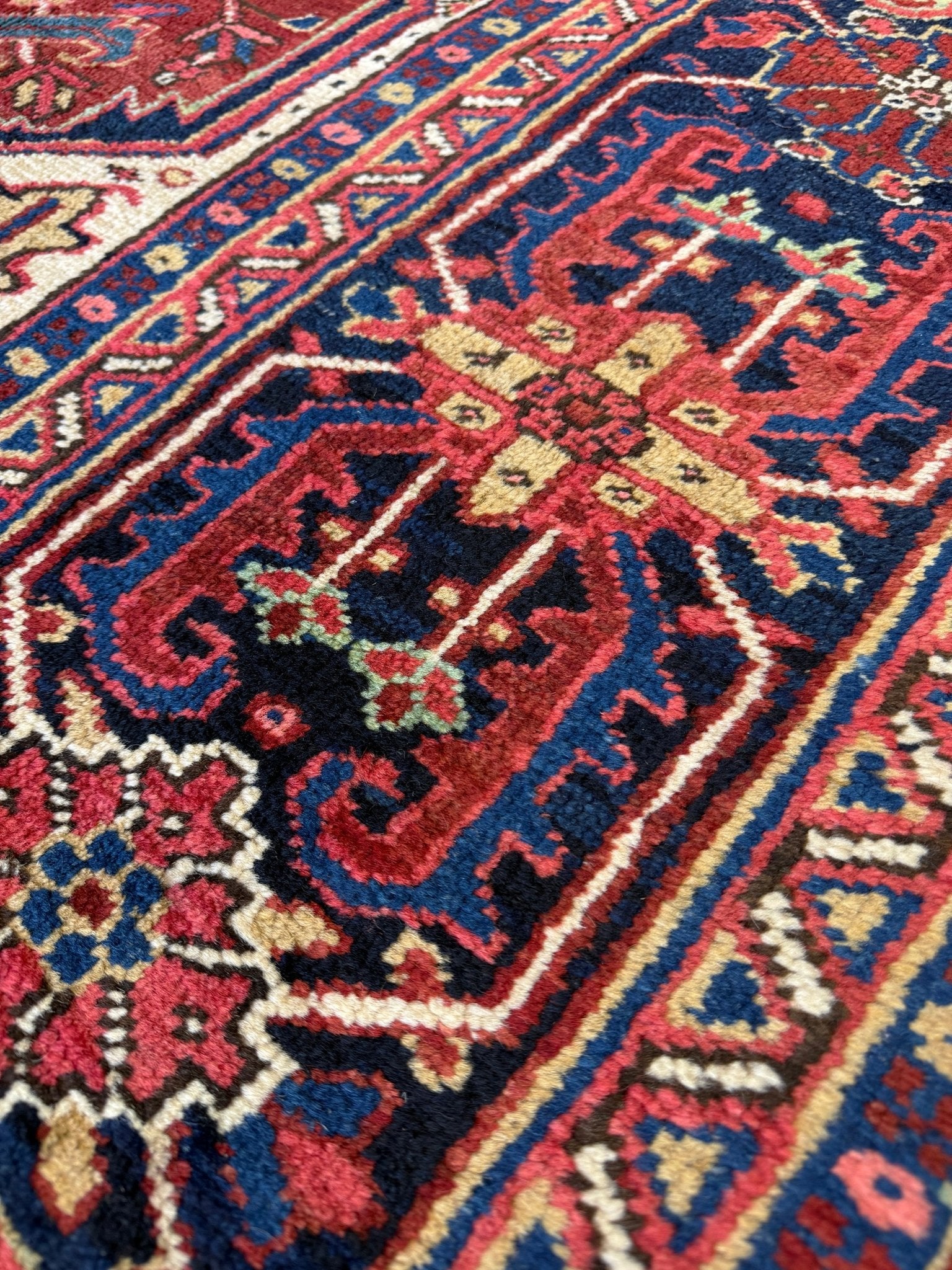 Close-up of a patterned rug with red, blue, and beige colors. 10x14 oversize handmade Persian Heriz vintage rug madder red and navy — shown in living room at Indigo Rugs, Burlingame — San Francisco Bay Area with free shipping