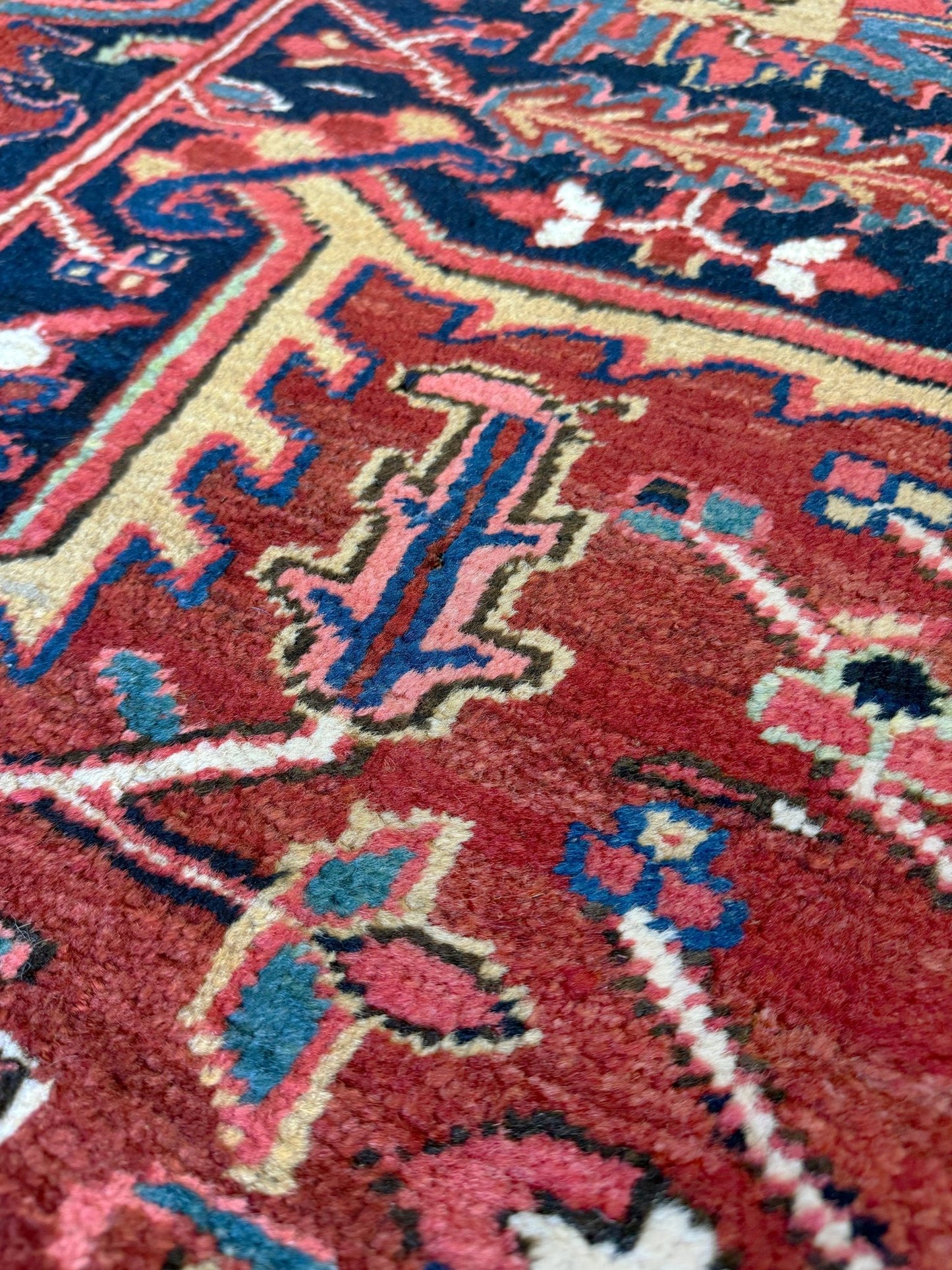 Close-up of a patterned rug with red, blue, and beige colors. 10x14 oversize handmade Persian Heriz vintage rug madder red and navy — shown in living room at Indigo Rugs, Burlingame — San Francisco Bay Area with free shipping
