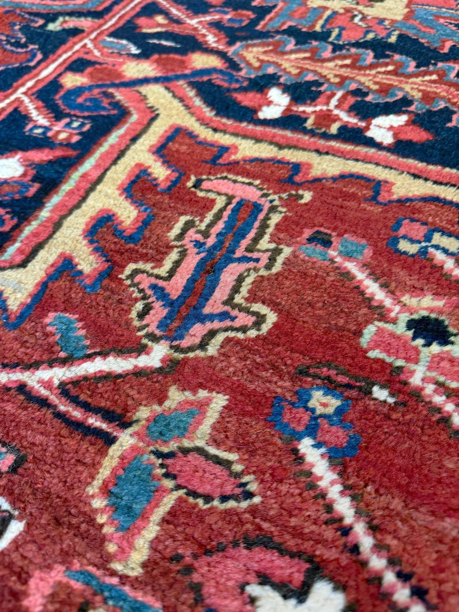Close-up of a patterned rug with red, blue, and beige colors. 10x14 oversize handmade Persian Heriz vintage rug madder red and navy — shown in living room at Indigo Rugs, Burlingame — San Francisco Bay Area with free shipping