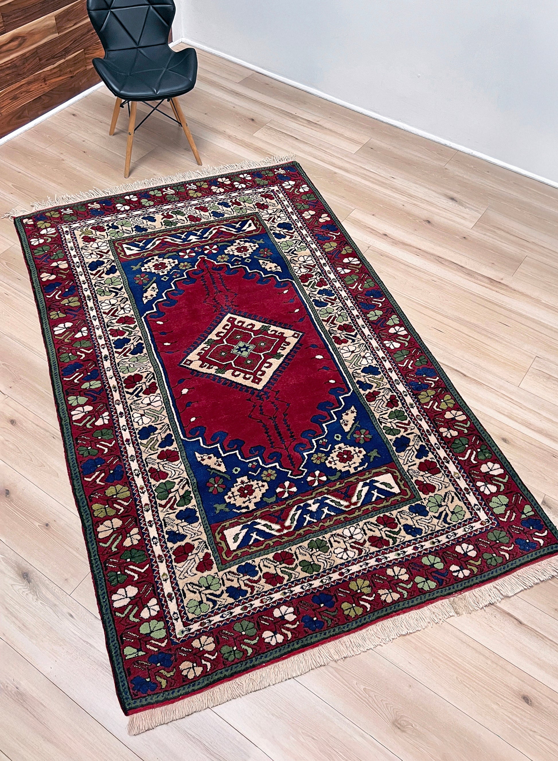 Decorative rug with intricate patterns on a wooden floor. crimson red vibrant anatolian turkish vintage rug 5x7 traditional handmade village wool rug blue medallion floral border plush pile indigo rugs san francisco bay area