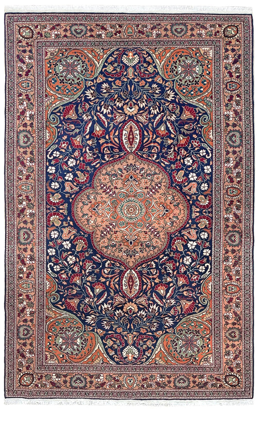 A traditional Persian-style area rug with a large central medallion, featuring a navy blue field, a peach and orange central medallion, and intricate floral motifs in red, green, beige, and white throughout the borders. 5x7 Navy Kayseri Turkish rug with peach medallion, floral vines, handmade wool from Indigo Rugs Burlingame Bay Area.