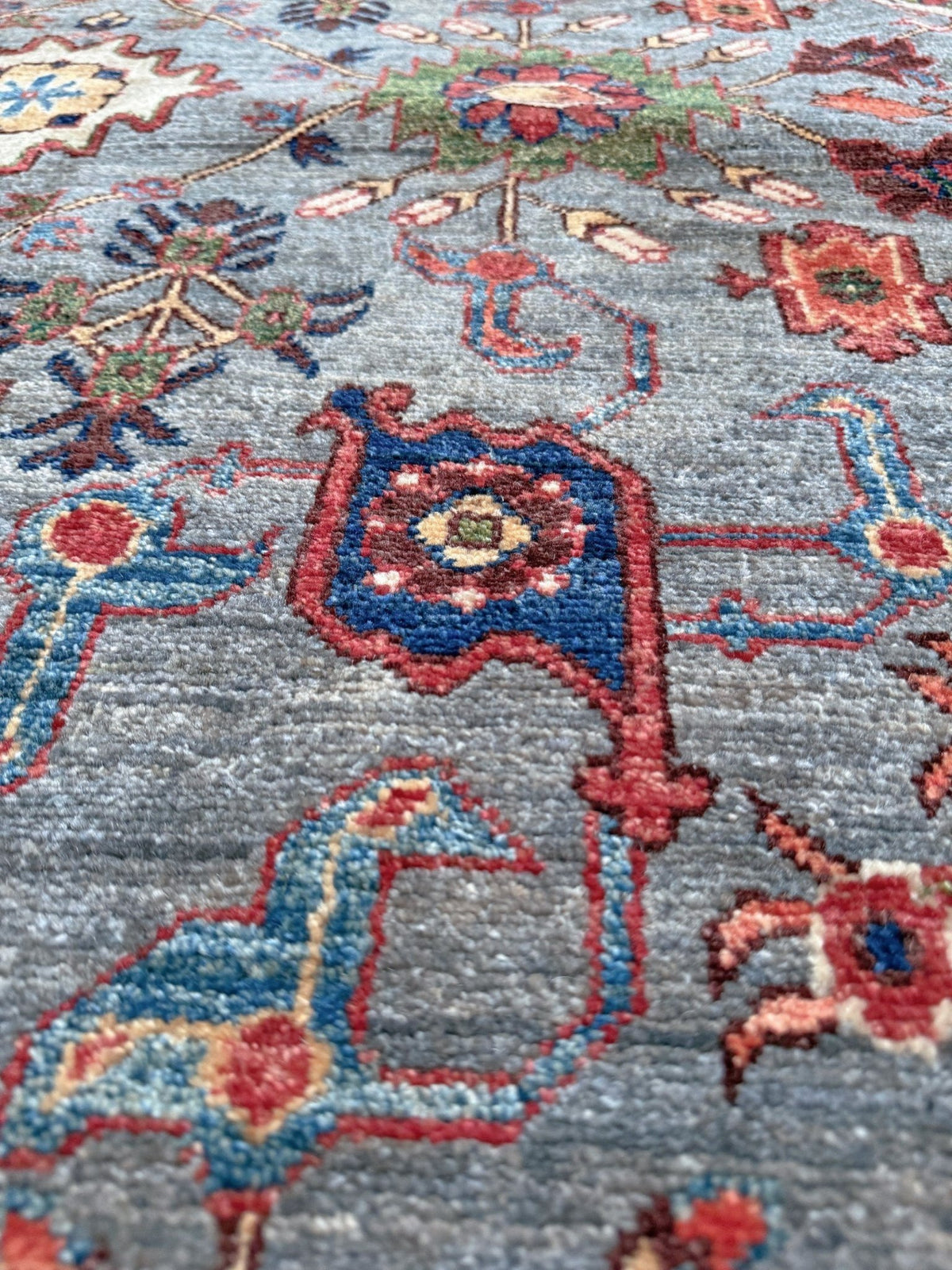 Close-up of a traditional patterned area rug with a blue-gray background and motifs in red, blue, pink, and beige. Blue gray Bijar Turkish rug with deep navy border, floral geometric motifs, handmade wool 7x10 from Indigo Rugs Burlingame CA Bay Area