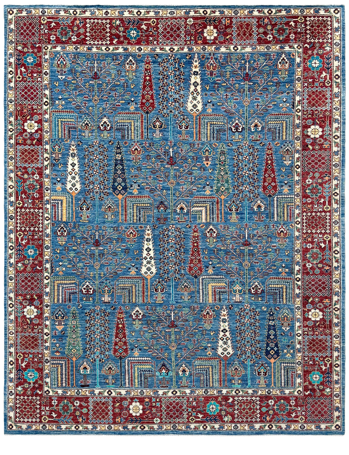A traditional Persian-style area rug with a complex geometric and floral pattern, featuring a dominant blue center field, a deep red border, and cream accents. Blue Tree of Life 9x12 rug with sky blue field, deep crimson border, cypress trees, floral motifs, handmade wool from Indigo Rugs Burlingame Bay Area.