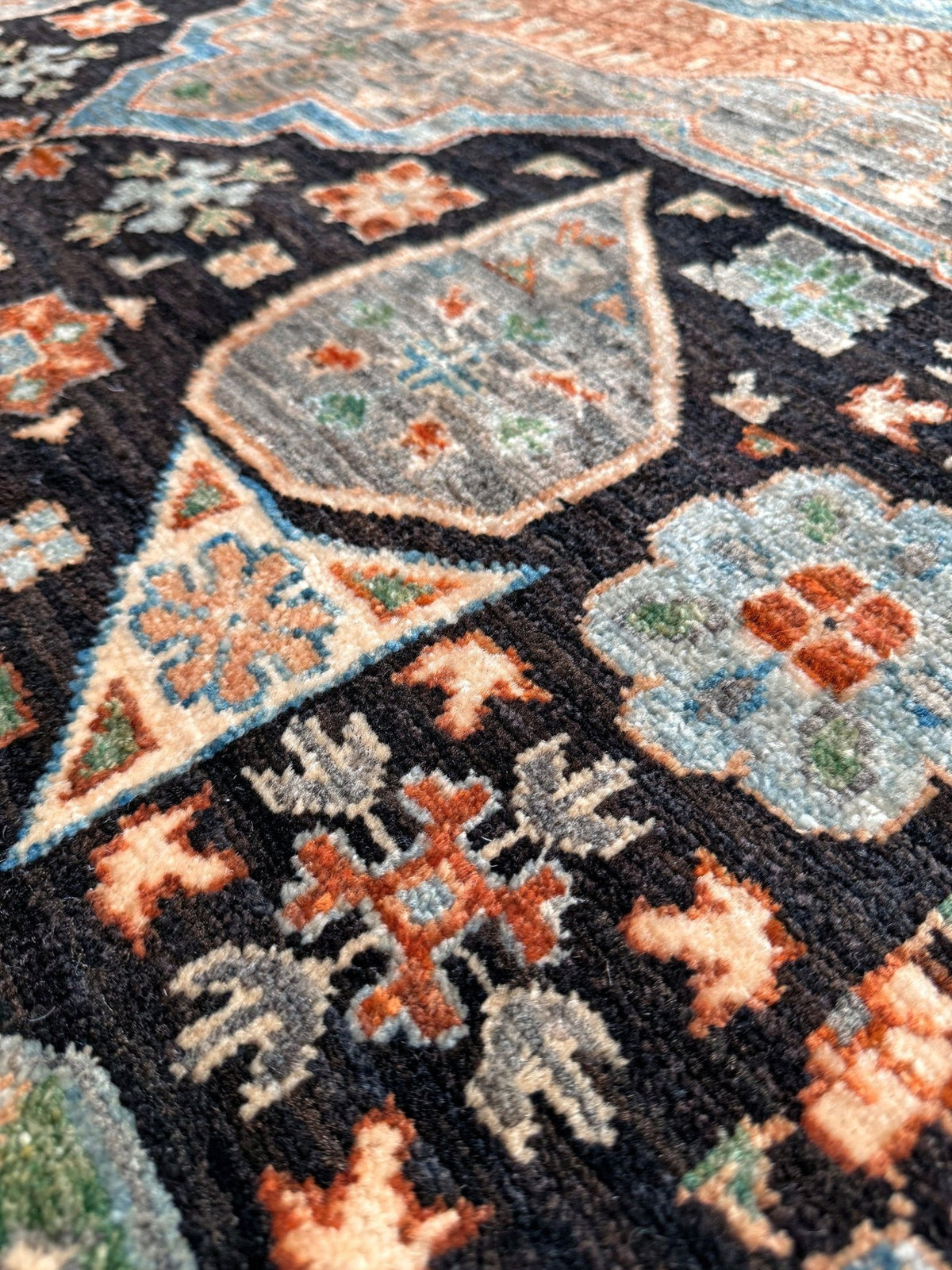Close-up of a traditional patterned rug with a black base and geometric motifs in beige, rust orange, light blue, and muted green.