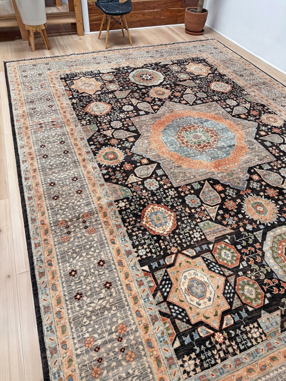 A large traditional area rug with an intricate geometric and floral medallion pattern, shown laid out on a light wood floor in a room setting. 10x14 Charcoal and peach Sultanate Mamluk rug with large central medallion, geometric floral motifs, handmade Turkish wool from Indigo Rugs Burlingame, SF Bay Area.