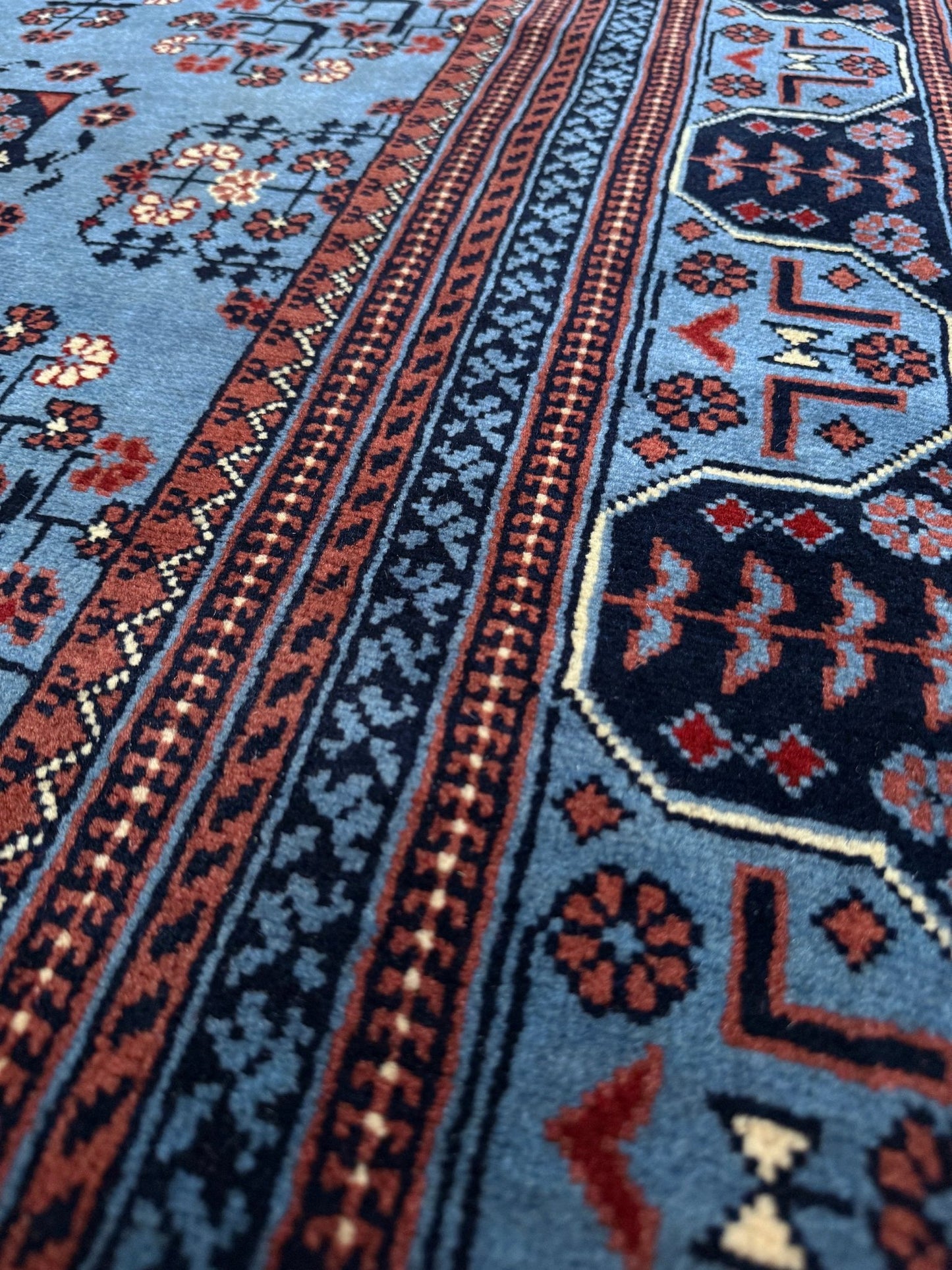 Close-up of 9x12 Handmade Turkmen rug with a baby blue ground, featuring traditional geometric motifs in brown, midnight blue, terracotta crafted from silky Merino wool with a luxurious sheen, available with free shipping from the best handmade rug shop Burlingame CA San Francisco Bay Area.