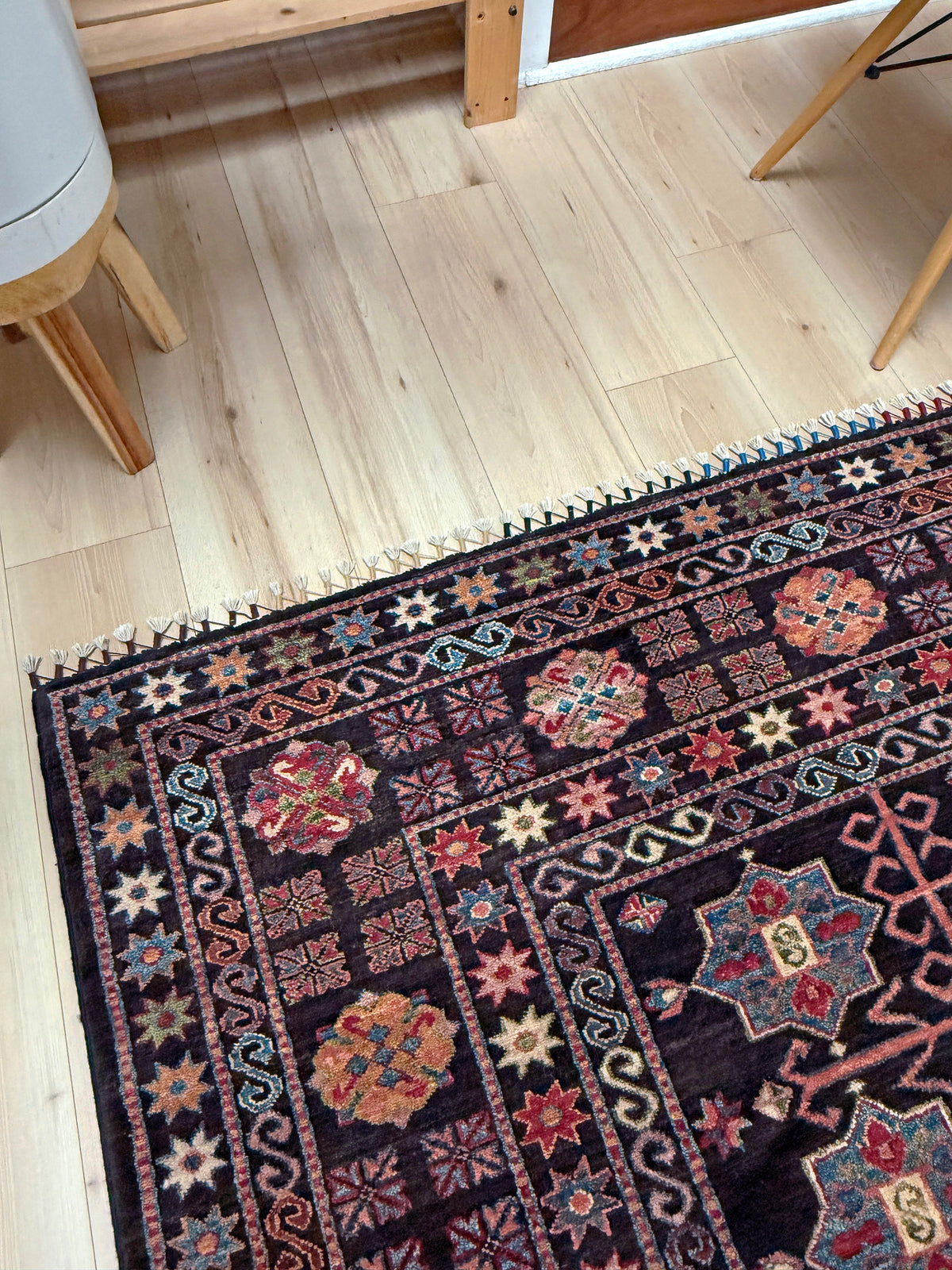 A dark brown traditional Persian-style area rug with intricate multicolor floral and geometric patterns, laid out on a light wood floor in a room setting.