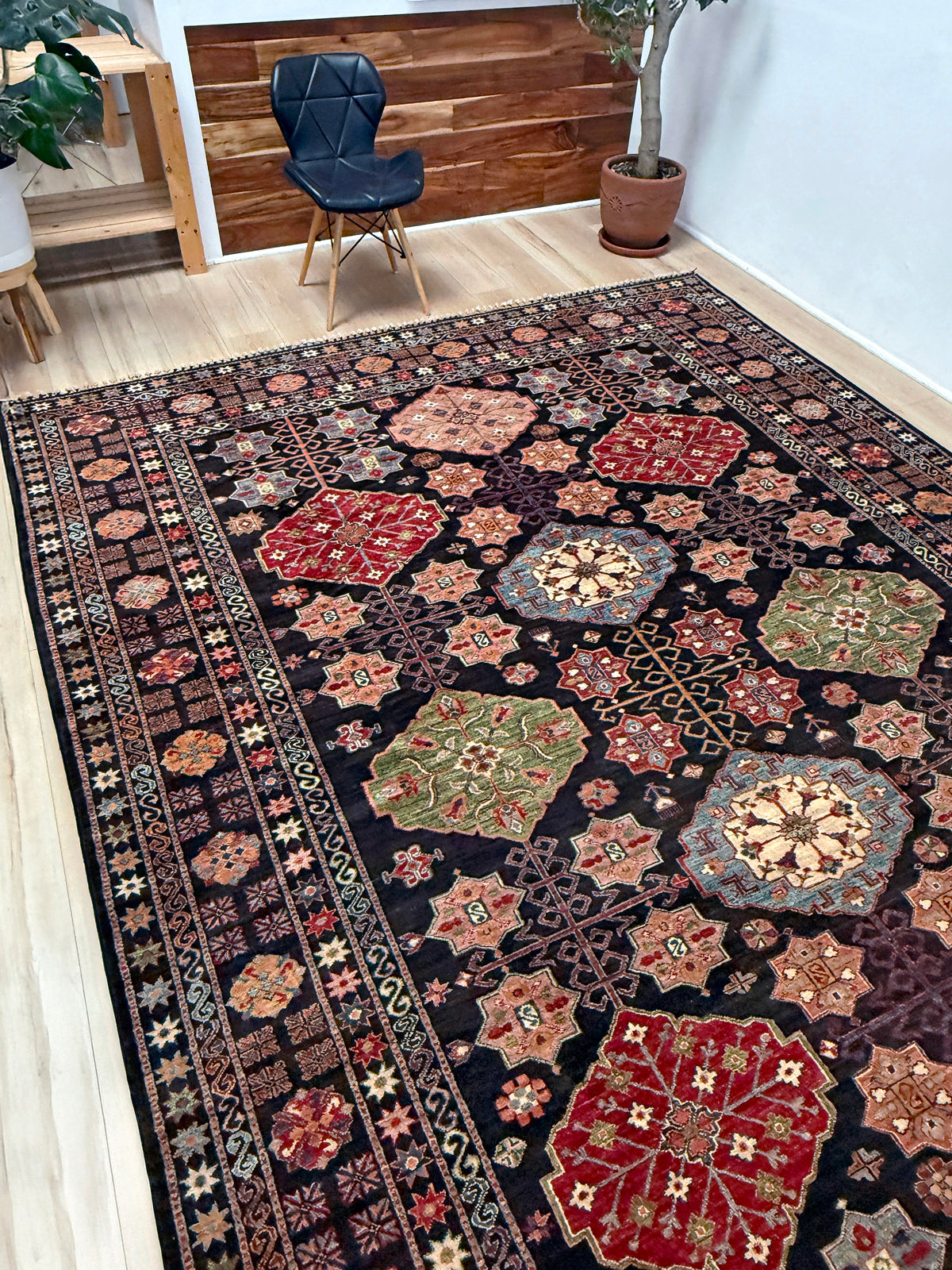 A large rectangular area rug with an intricate traditional geometric and floral pattern, laid out on a light wood floor in a modern room setting.