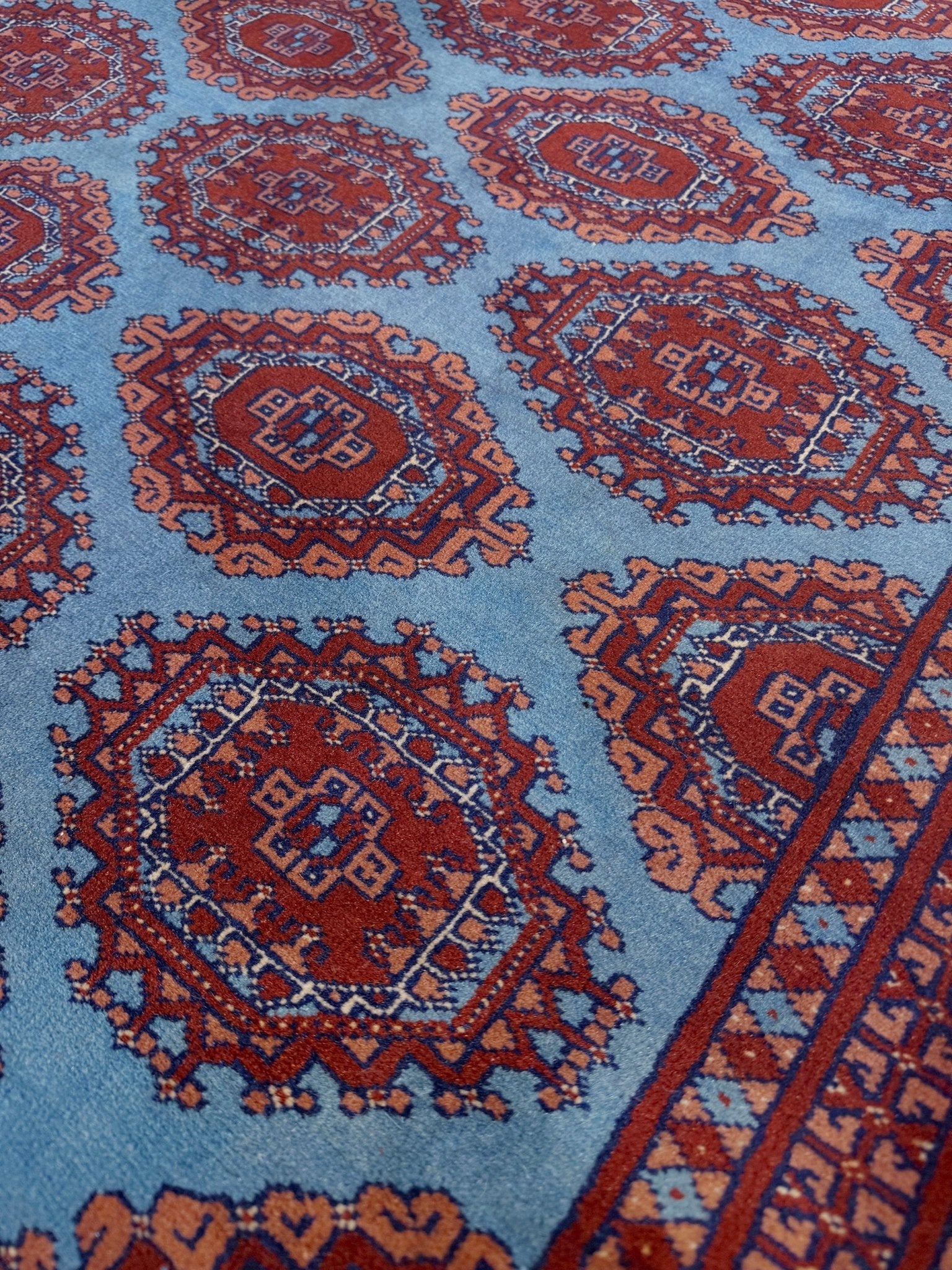 Vintage Uzbek Bukhara rug with sky blue field and repeating brick red gul motifs, navy borders, large handmade merino wool area rug 10x14 with velvety pile from Indigo Rugs Burlingame Bay Area