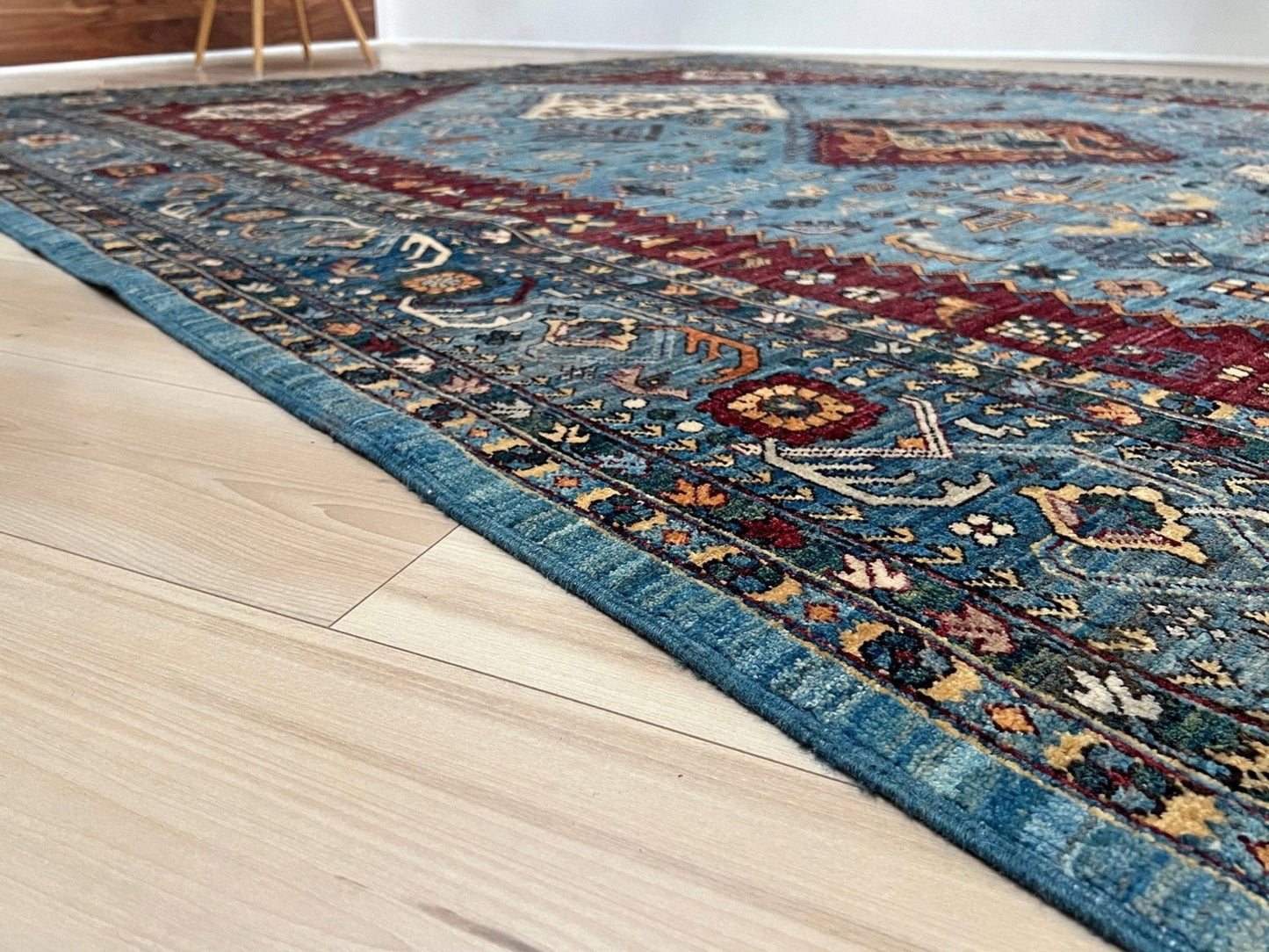 Decorative rug with intricate patterns on a wooden floor. large handmade sky blue and deep maroon turkish rug 9x12 geometric medallion design transitional tribal wool rug soft pile indigo rugs burlingame san francisco bay area