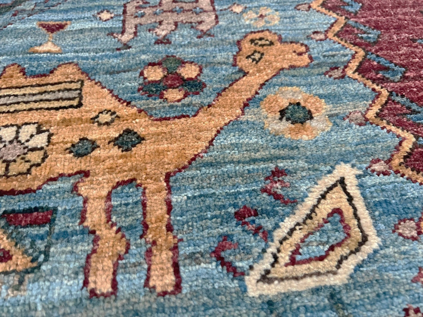 Close-up of a rug with a camel design on a blue background. large handmade sky blue and deep maroon turkish rug 9x12 geometric medallion design transitional tribal wool rug soft pile indigo rugs burlingame san francisco bay area