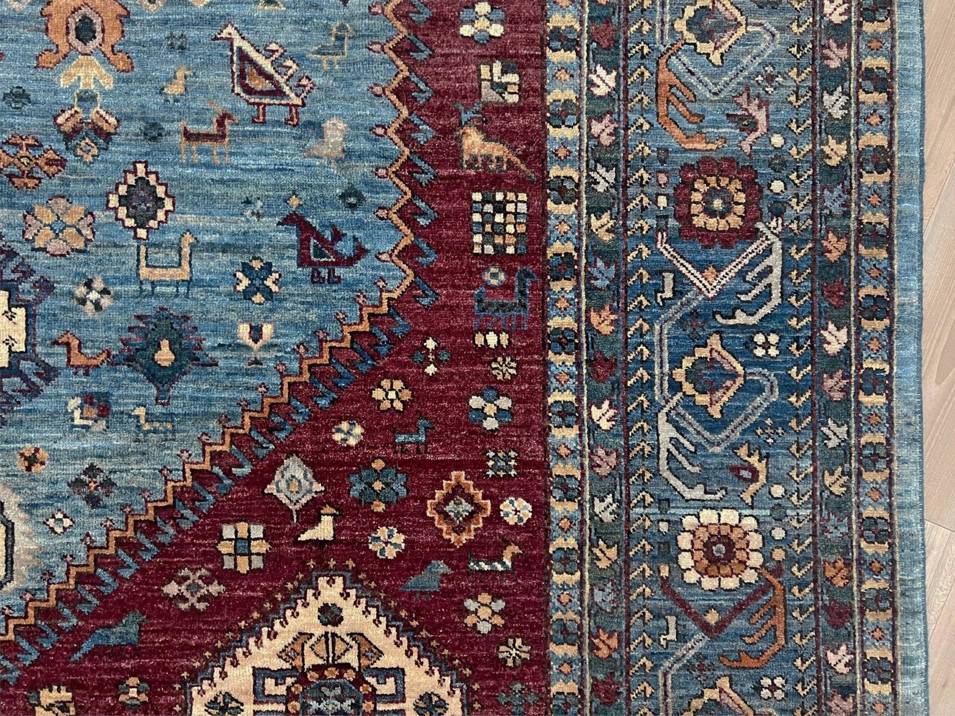 Close-up of a patterned rug with blue, red, and beige colors. large handmade sky blue and deep maroon turkish rug 9x12 geometric medallion design transitional tribal wool rug soft pile indigo rugs burlingame san francisco bay area