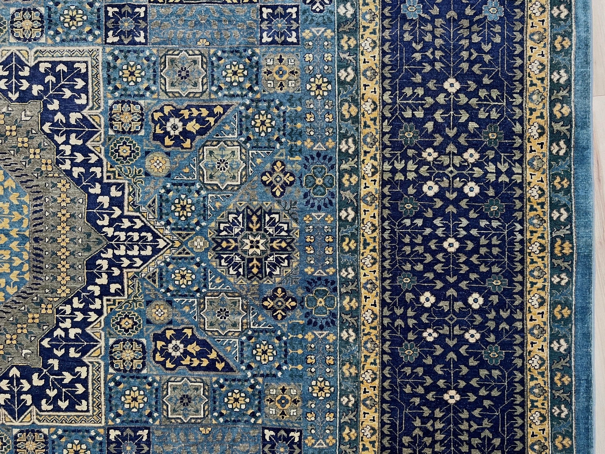 Decorative blue and gold rug with intricate patterns on a wooden floor. Brand new fine Mamluk rug 10x14 with navy, denim blue, and soft gold geometric medallion design, high knot density (50×50 ~156 KPSI), perfect for large living rooms and dining spaces. From Indigo Rugs, Burlingame — the best rug shop in the San Francisco Bay Area. Free shipping.