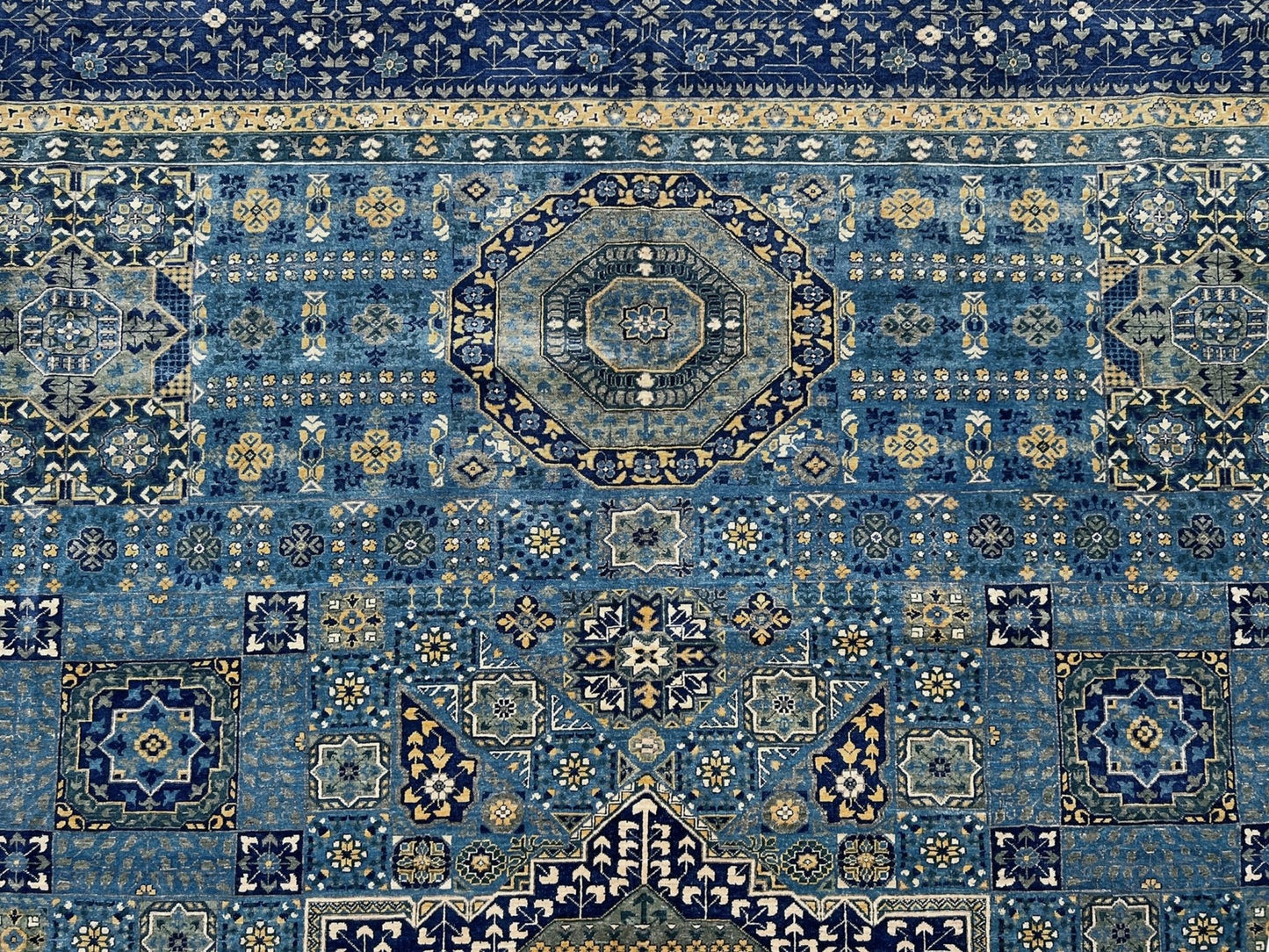 Close-up of a Decorative blue and gold rug with intricate patterns on a wooden floor. Brand new fine Mamluk rug 10x14 with navy, denim blue, and soft gold geometric medallion design, high knot density (50×50 ~156 KPSI), perfect for large living rooms and dining spaces. From Indigo Rugs, Burlingame — the best rug shop in the San Francisco Bay Area. Free shipping.