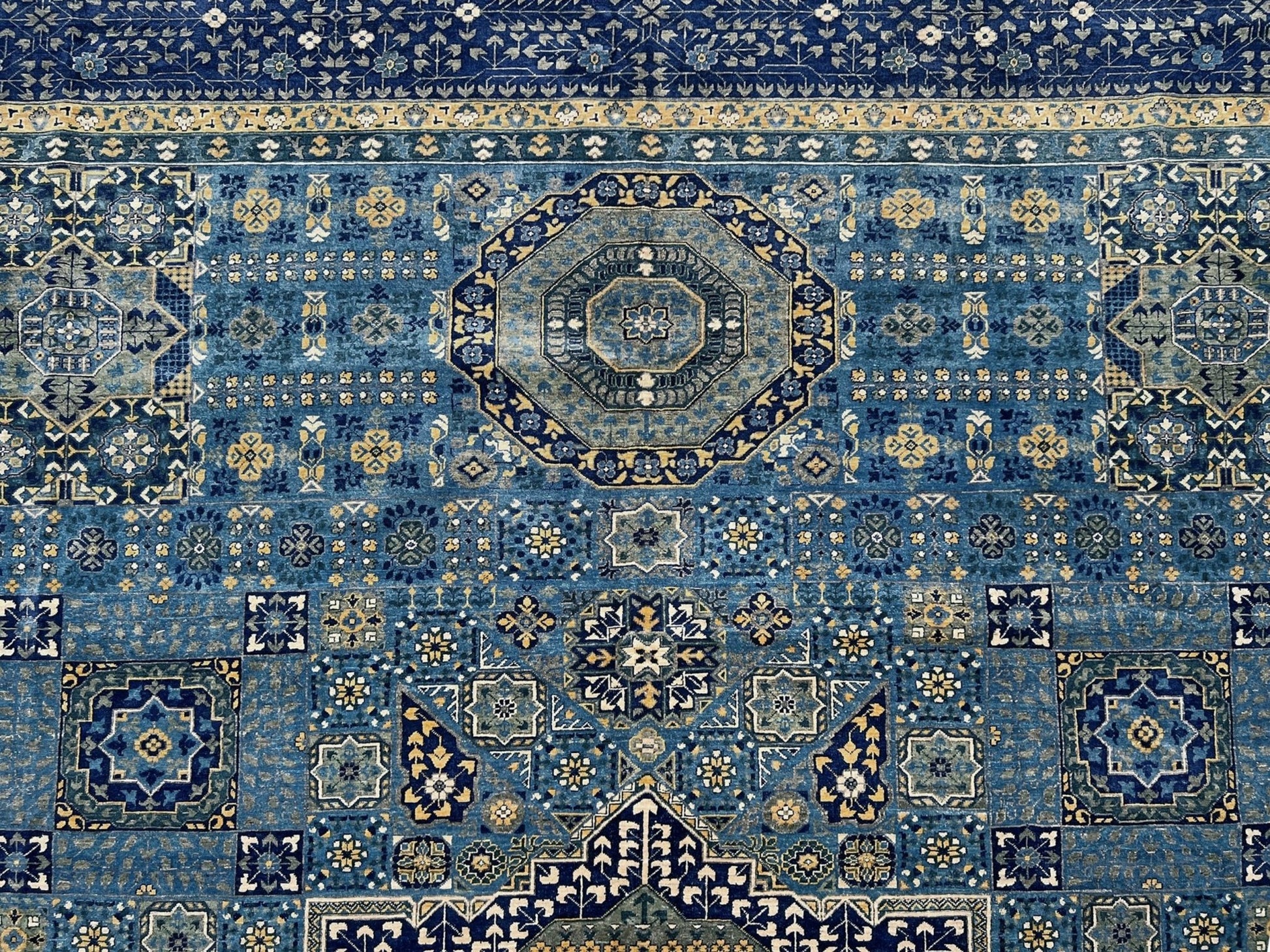 Close-up of a Decorative blue and gold rug with intricate patterns on a wooden floor. Brand new fine Mamluk rug 10x14 with navy, denim blue, and soft gold geometric medallion design, high knot density (50×50 ~156 KPSI), perfect for large living rooms and dining spaces. From Indigo Rugs, Burlingame — the best rug shop in the San Francisco Bay Area. Free shipping.