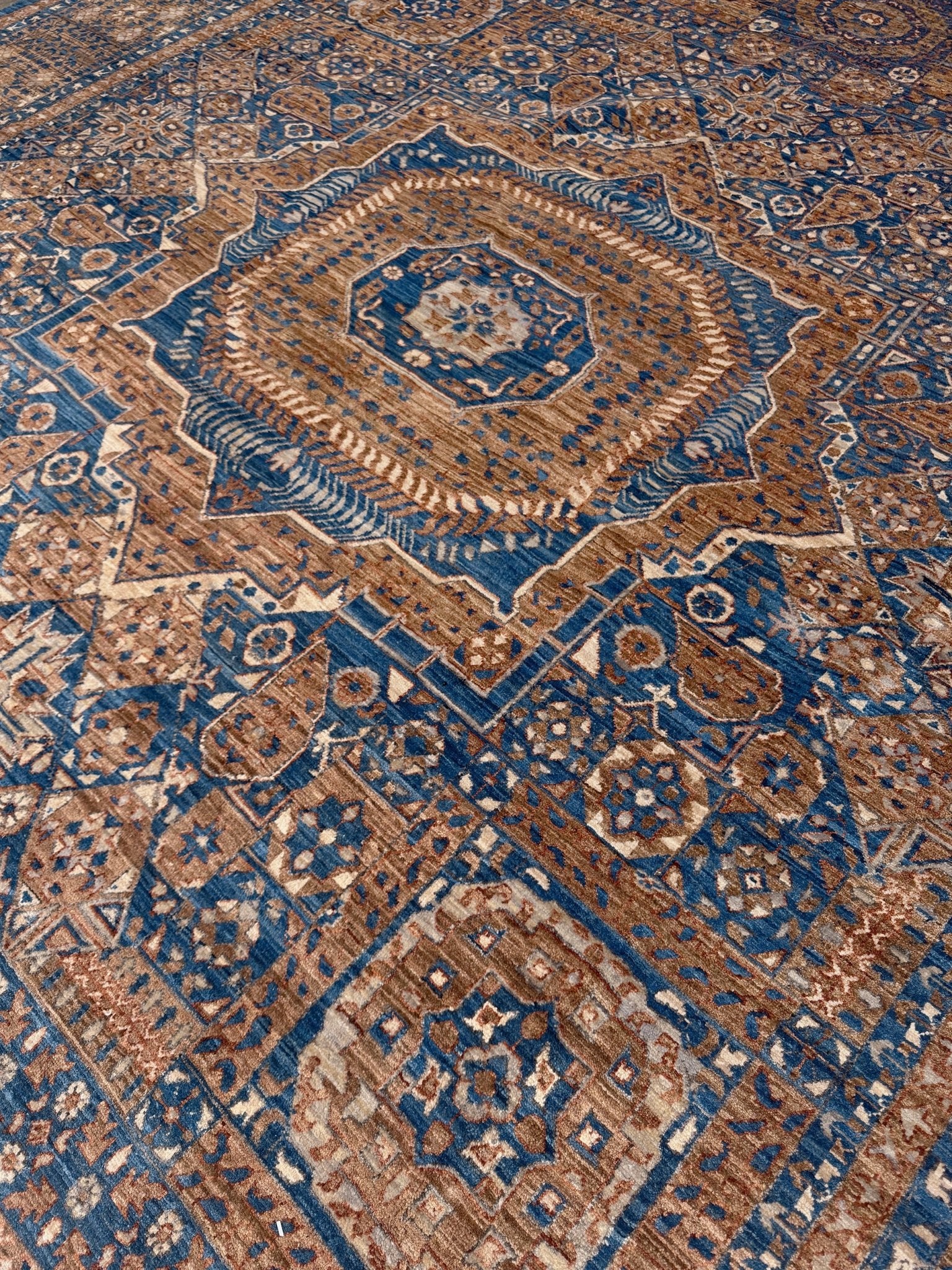 Close-up of a blue and brown patterned rug. 50x50 handmade Mamluk rug with walnut brown field, denim blue geometric medallions, ivory and taupe details, traditional wool area rug 9x12 from Indigo Rugs Burlingame Bay Area.
