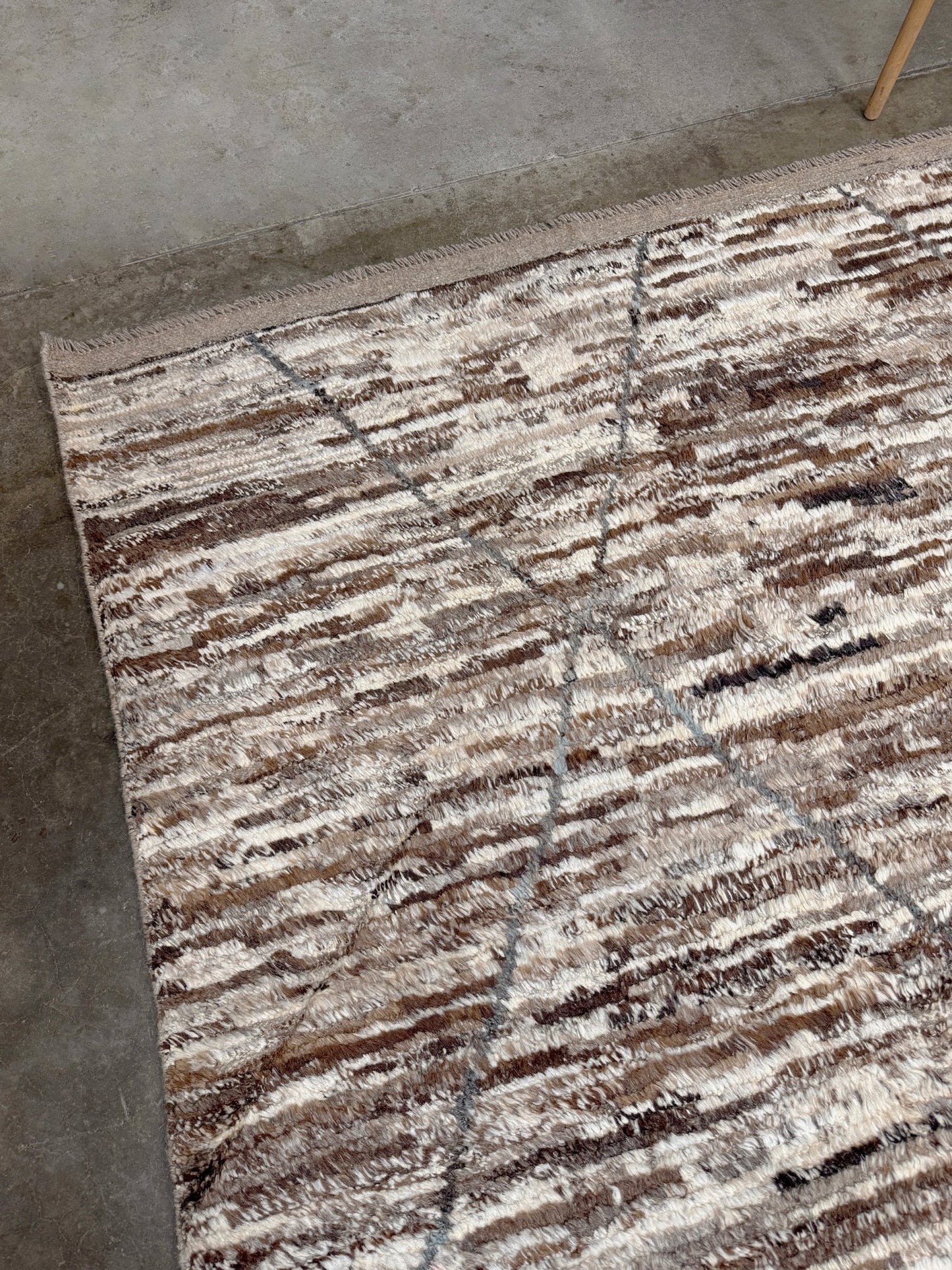 Textured area rug with brown and beige pattern on a concrete floor. Square 9x10 handmade Turkish Tulu rug with ivory and brown textured wool pile, subtle diamond lattice design — shown at Indigo Rugs, Burlingame — San Francisco Bay Area with free shipping