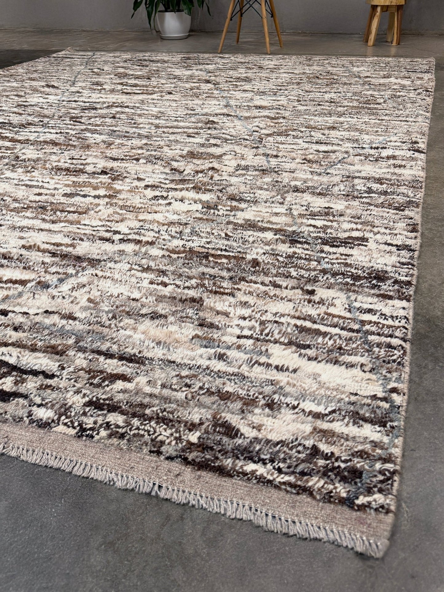 Textured area rug with a pattern on a gray floor. Square 9x10 handmade Turkish Tulu rug with ivory and brown textured wool pile, subtle diamond lattice design — shown at Indigo Rugs, Burlingame — San Francisco Bay Area with free shipping