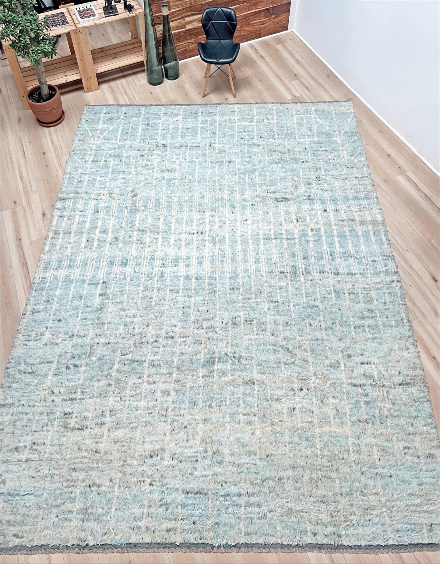 Light blue woven rug on a wooden floor with a chair and plants in the background. Moroccan Shag minimalist rug wool handmade 10x14 large area rug. Rug shop San Francisco Bay Area. Buy rug online.